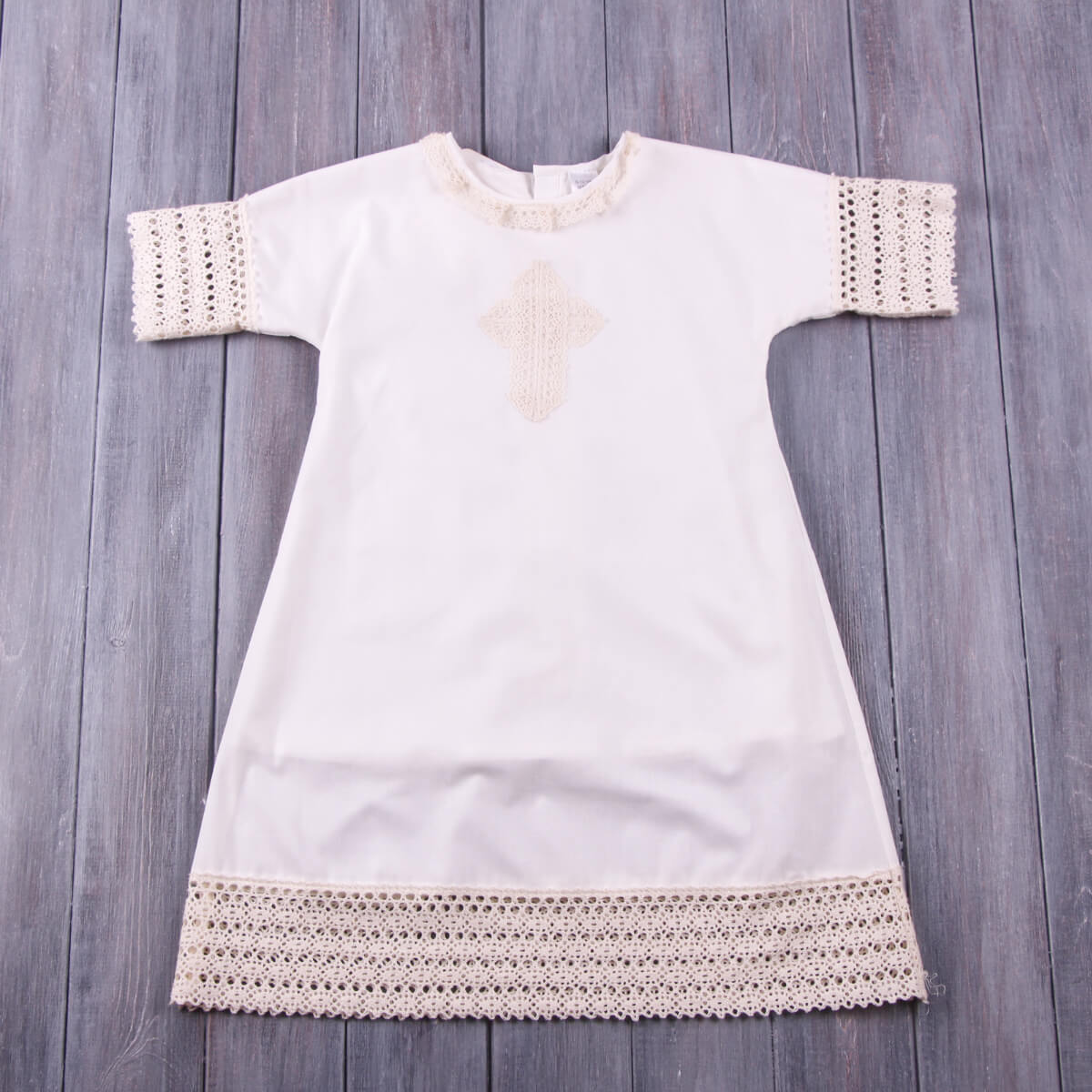 Baptism Gown with lace details on a wooden surface