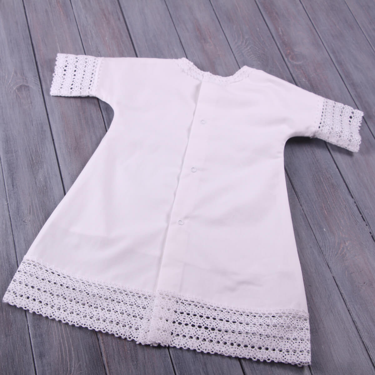 Baptism Gown with lace details on a wooden surface