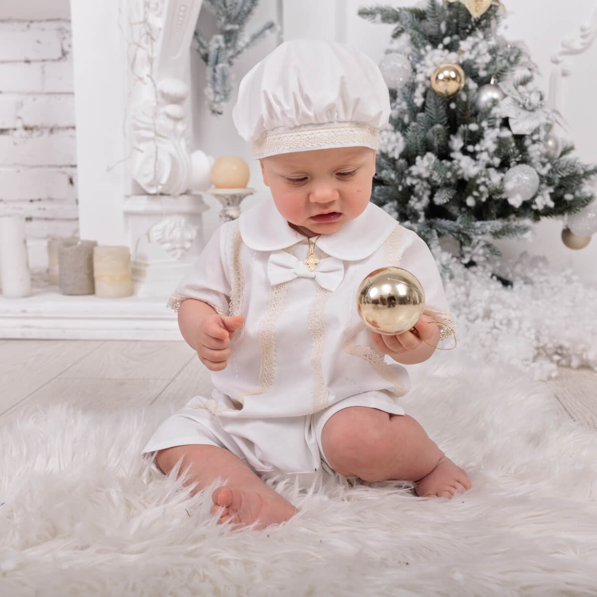 Baby in a Baby Boy Christening Romper a gold ornament in a festive setting with a Christmas tree.
