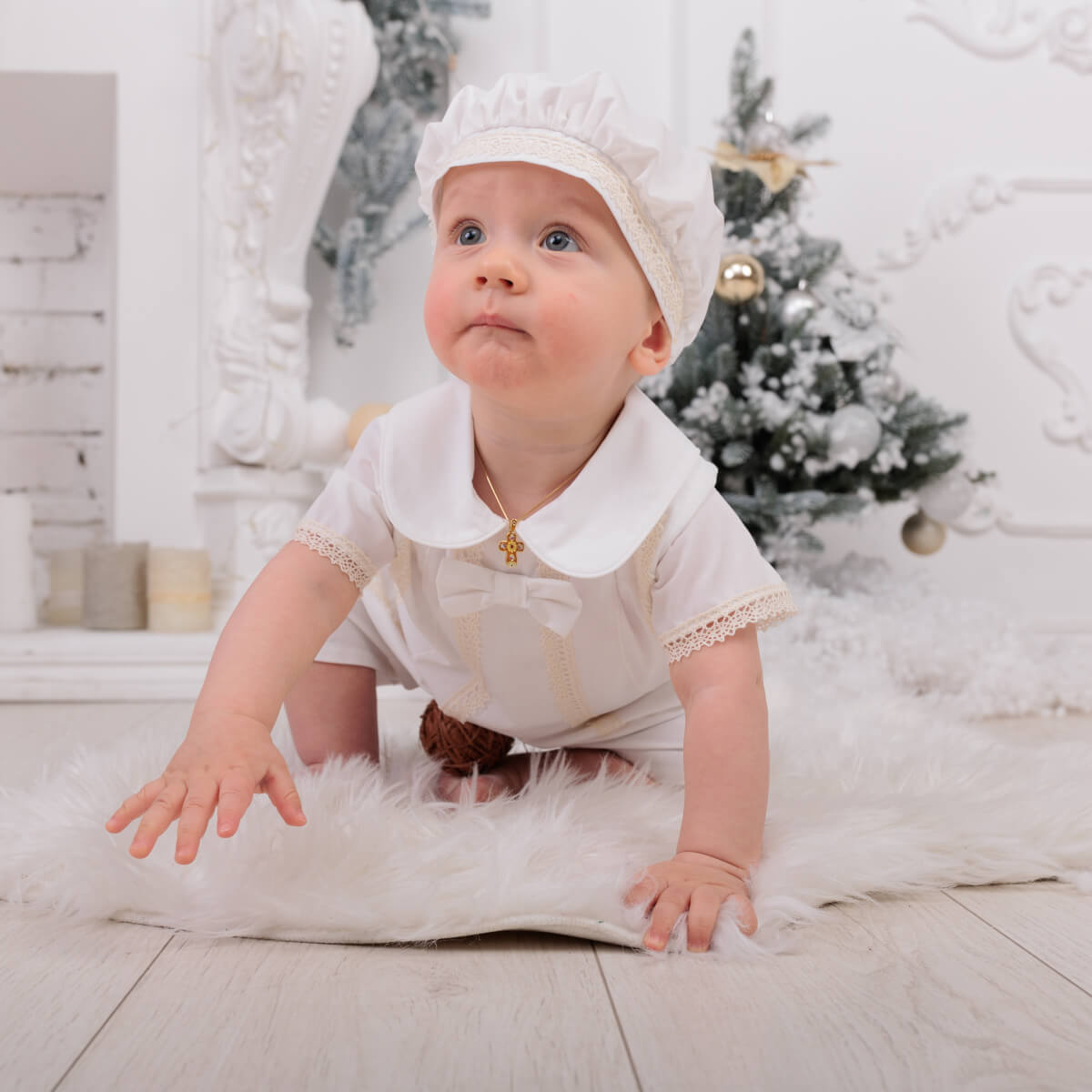 Baby in a Baby Boy Christening Romper with a gold necklace, sitting on a fluffy white rug in a decorated room.
