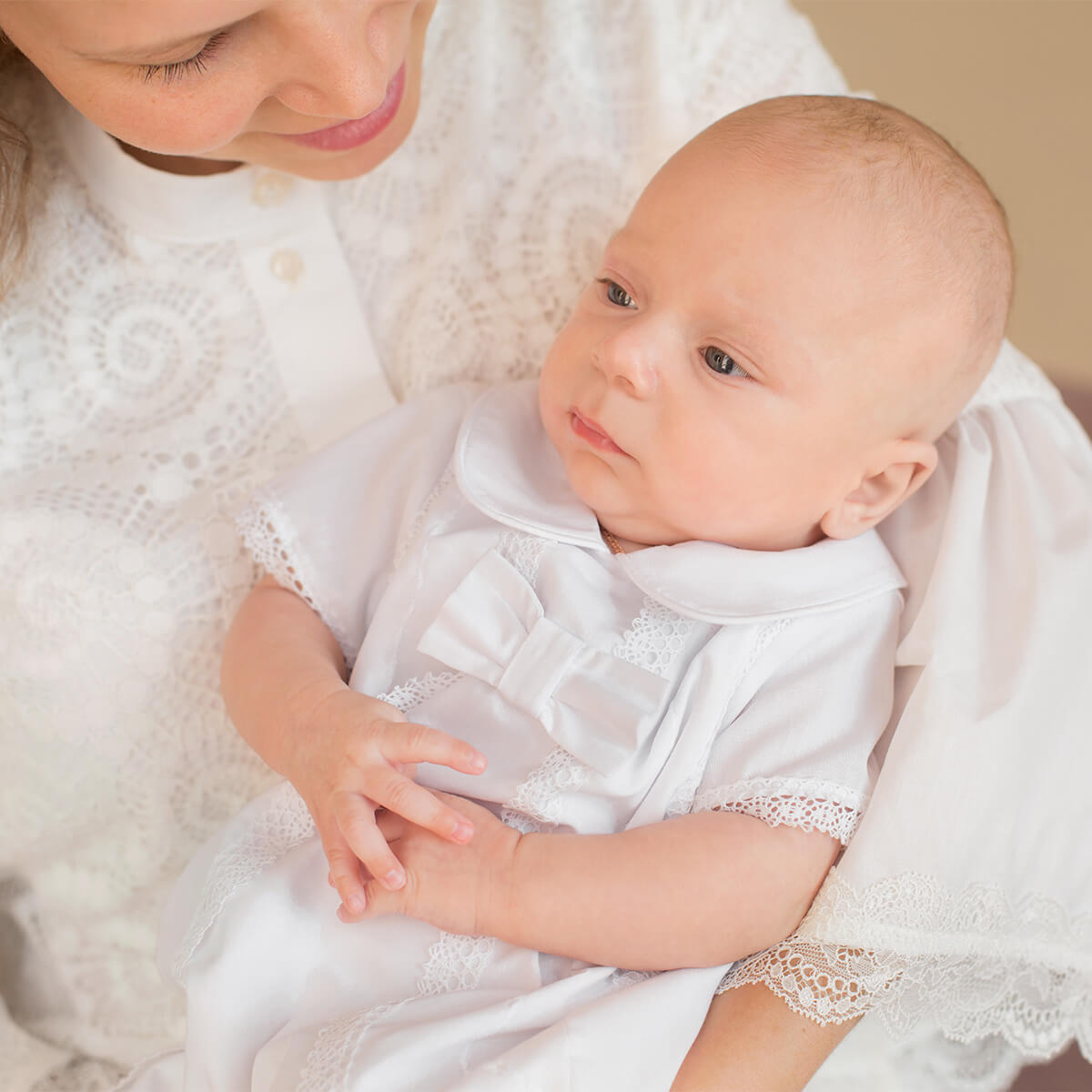 Baby in a Baby Boy Christening Romper being held by a person in a textured white garment.