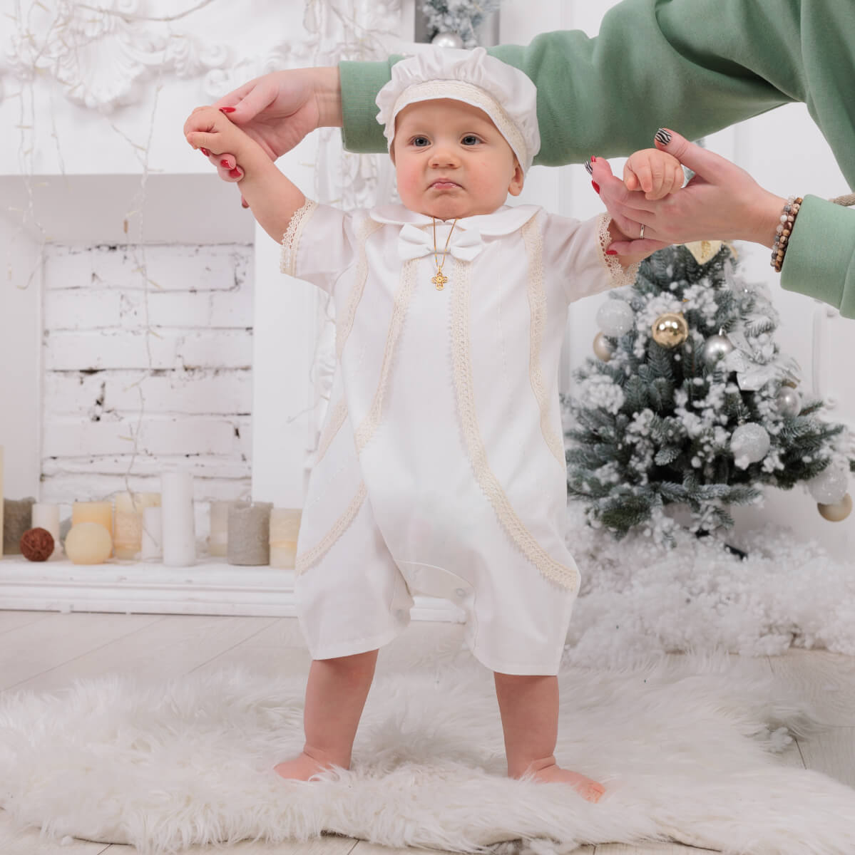Baby in a Baby Boy Christening Romper with a green coat holding hands, Christmas tree in the background