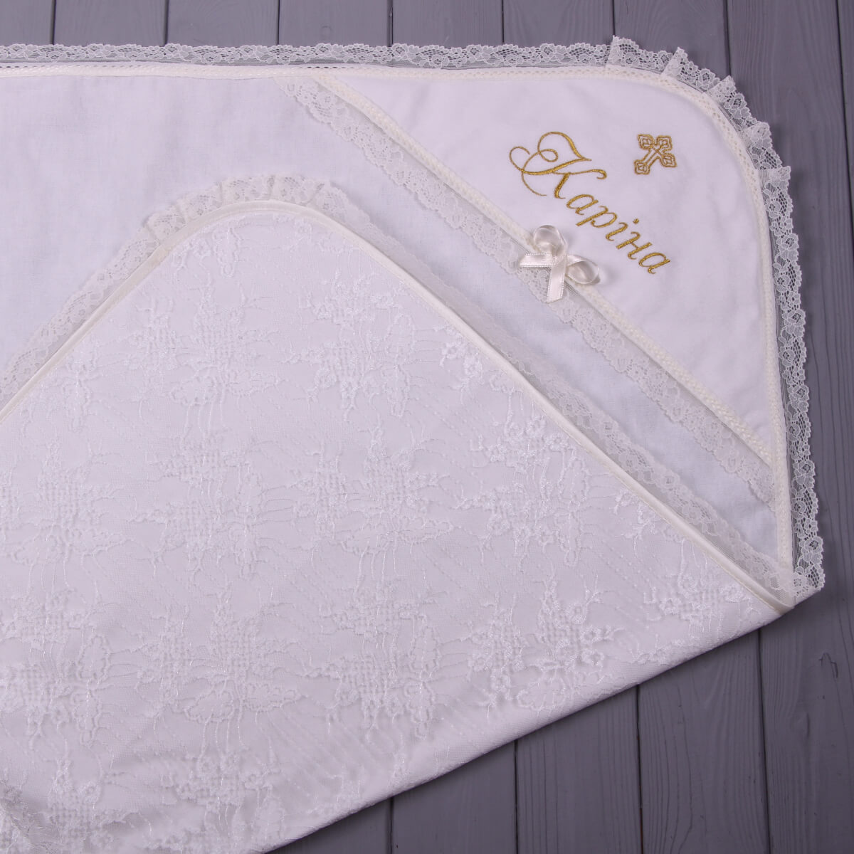 White baby blanket with lace trim and embroidered name on a wooden surface