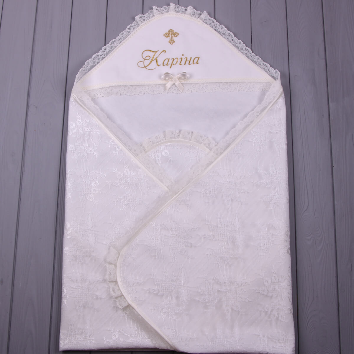 Ivory baby blanket with lace trim and embroidered name on a wooden surface