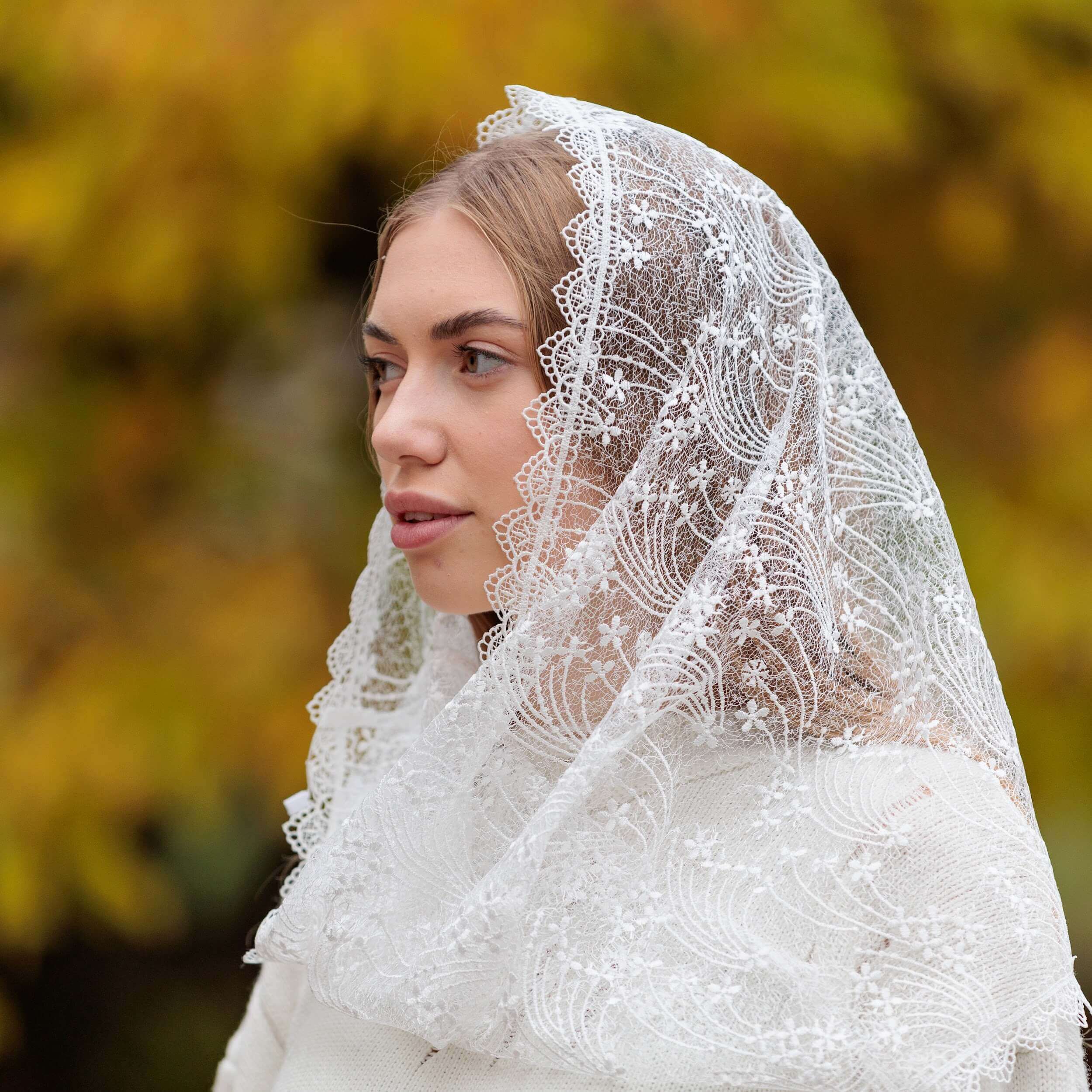 Woman wearing a Catholic Infinity Veil  against a blurred natural background