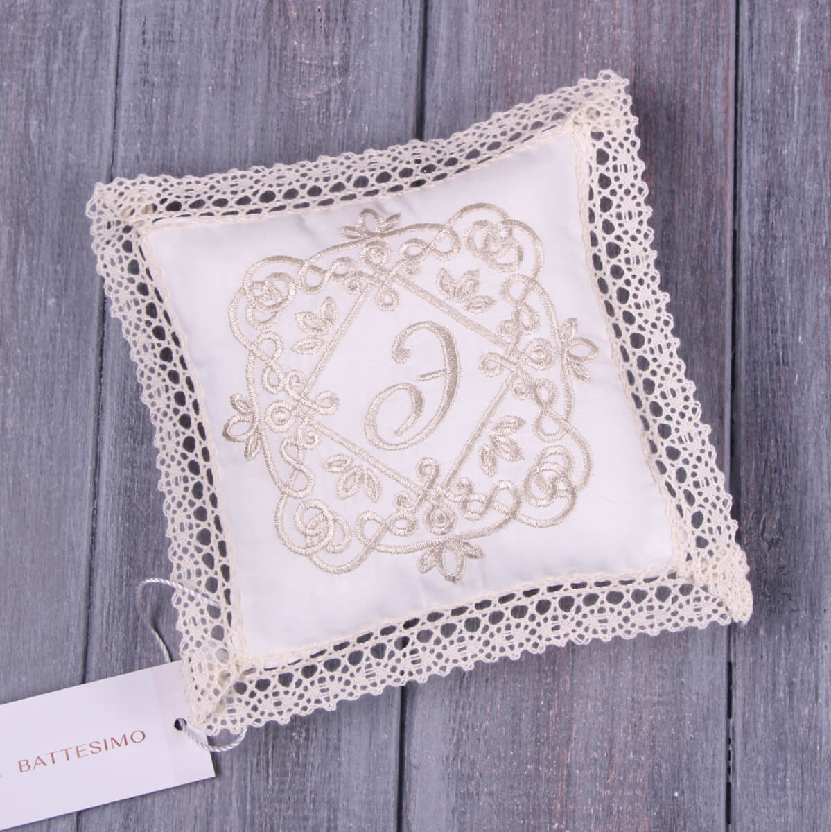 Baptism Ceremony Pillow with lace trim and embroidered letter 'D' on a wooden surface, featuring the brand 'Battesimo'.