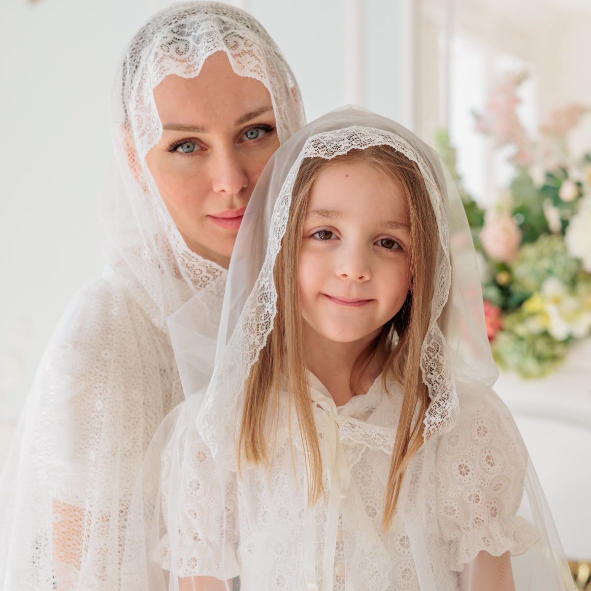 Woman and young girl wearing Catholic Church Mantilla  indoors with a blurred floral background
