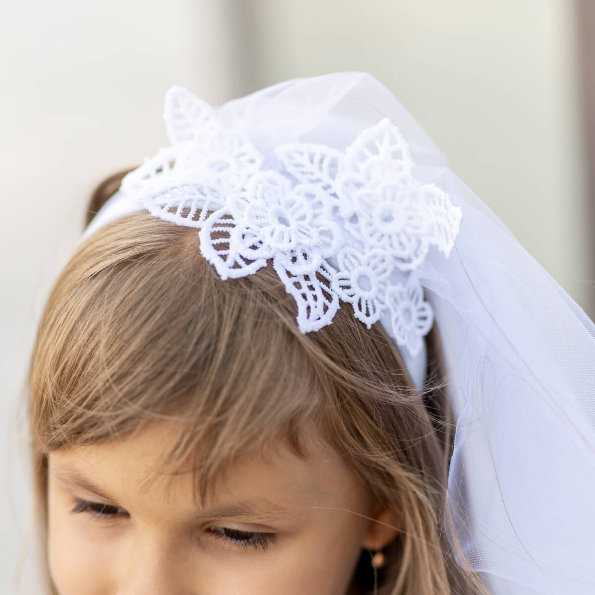 Young girl wearing a First Communion Veil with lace details and a matching veil.