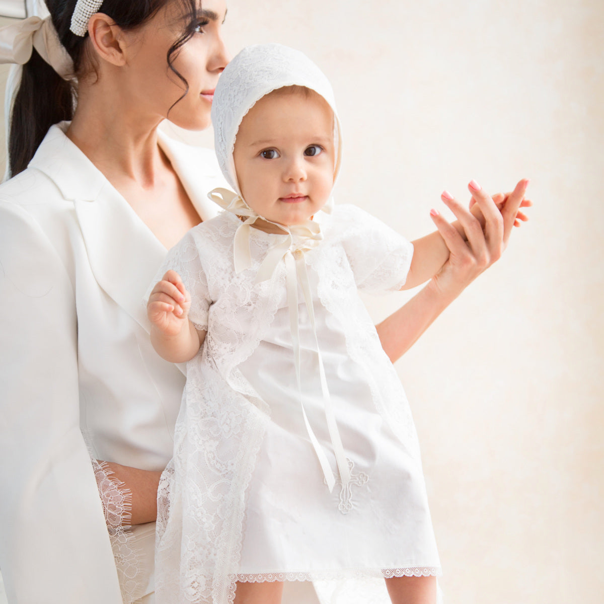 Woman holding a baby dressed inGirls Classic Baptism Gown against a light background