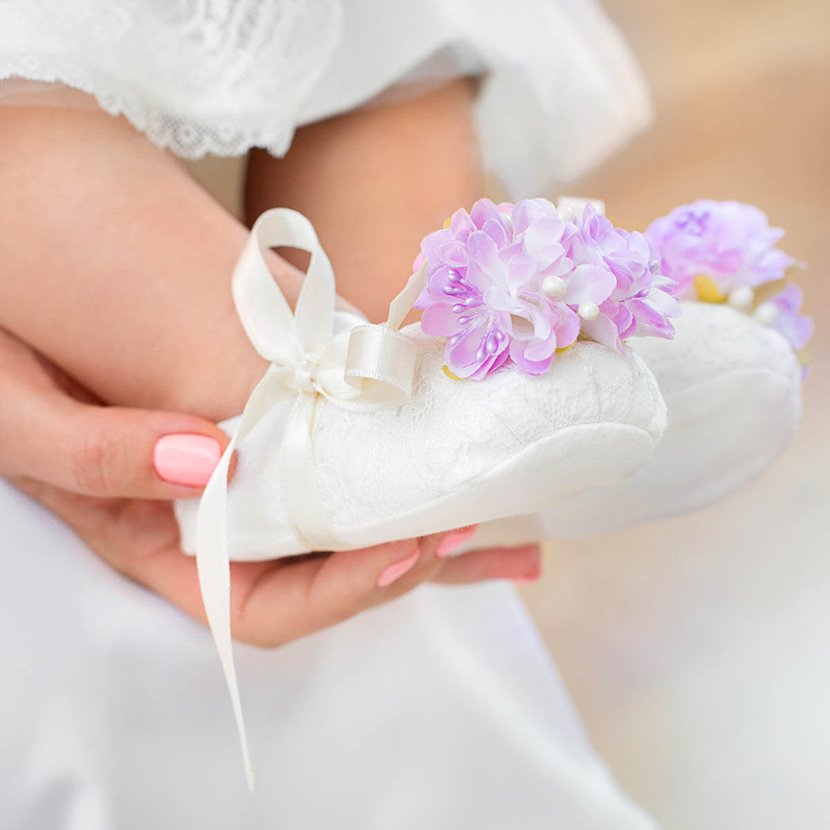 Christening Booties with pink flowers held by a hand against a blurred background