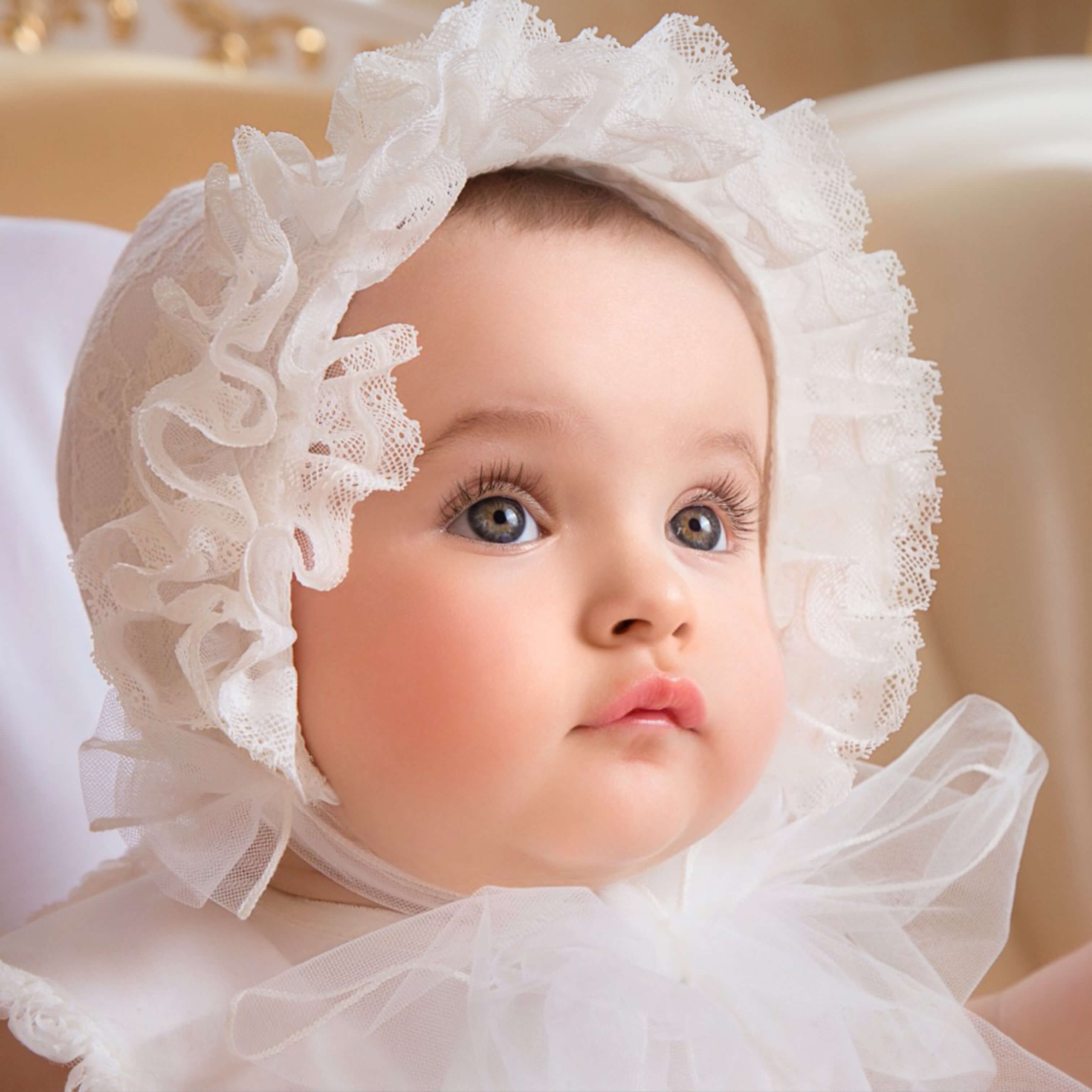 Baby wearing a  lace baptism bonnet with a soft focus background
