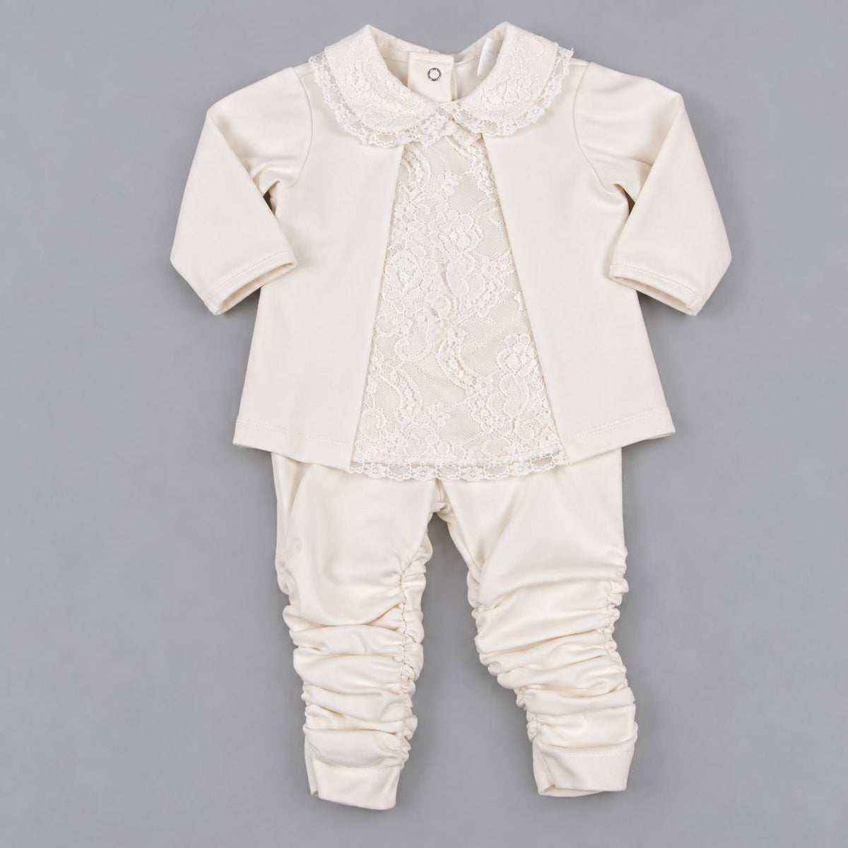 A baby girl's two-piece outfit in cream/off-white, featuring a long-sleeve cardigan with a lace front panel and ruffled collar, paired with matching ruched pants, laid flat on a gray background.