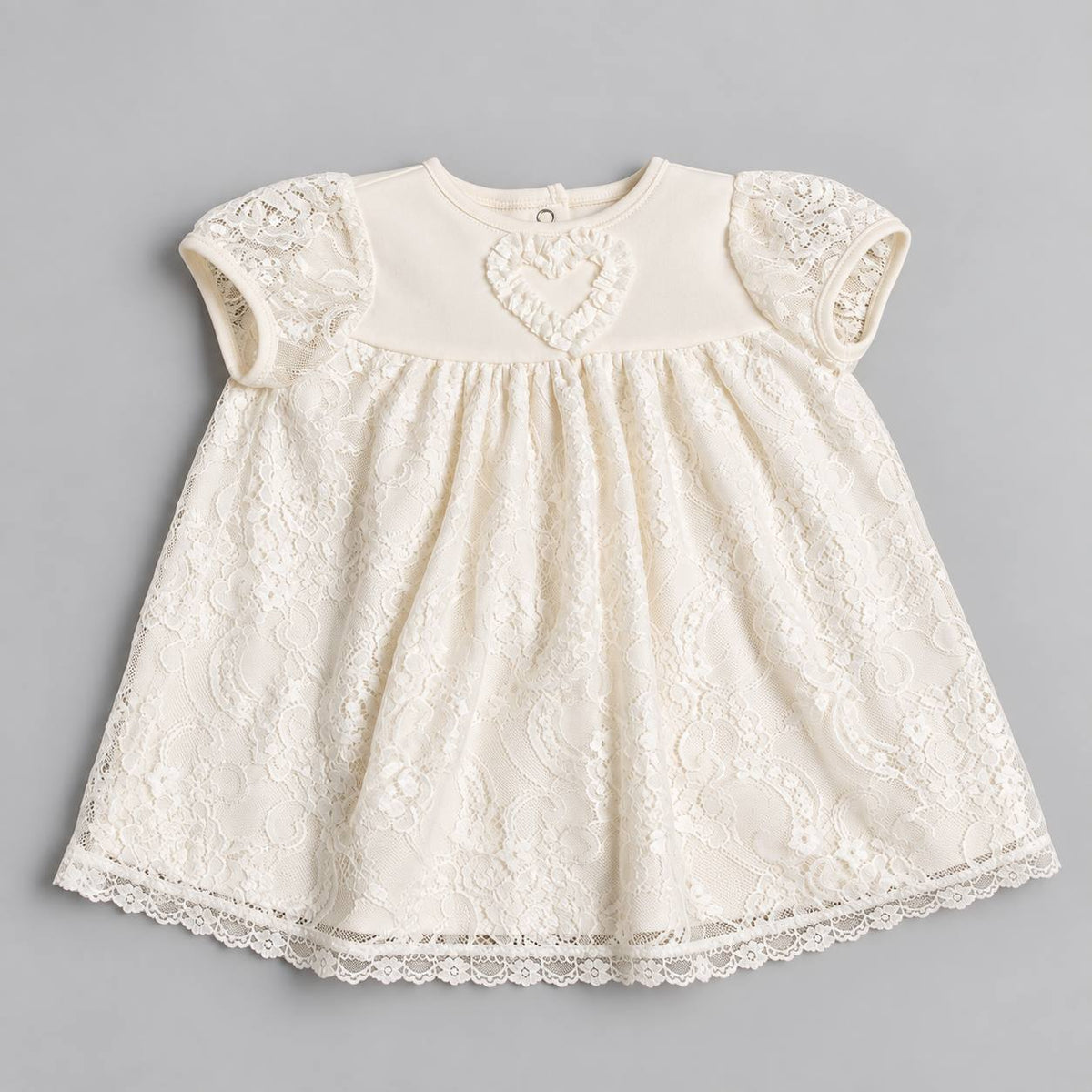 An ivory baby girl's dress featuring a solid cream bodice with a raised heart motif, short lace cap sleeves, and a matching lace hem, laid flat on a neutral gray background.