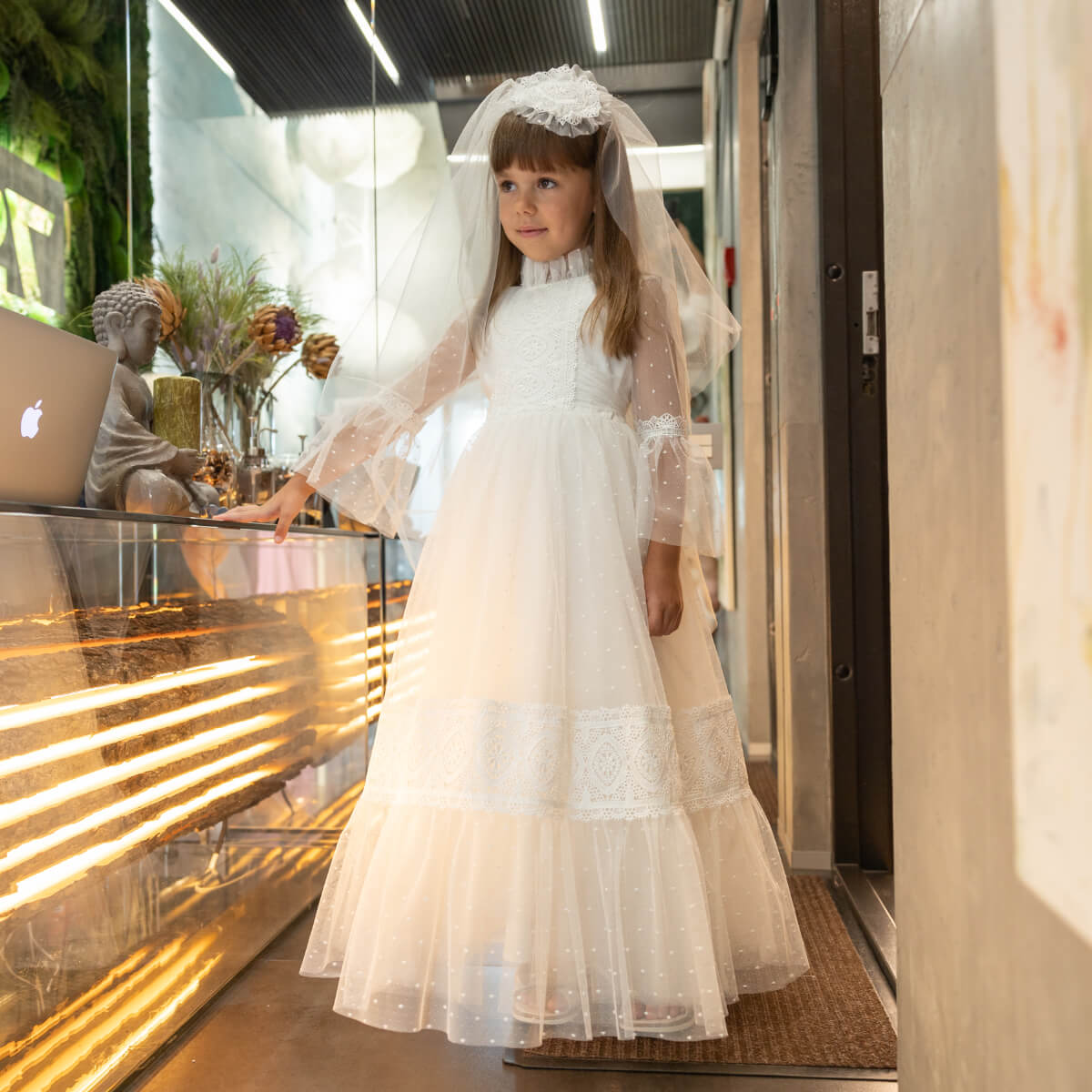 Young girl in a first communion dress with a veil standing in a store.