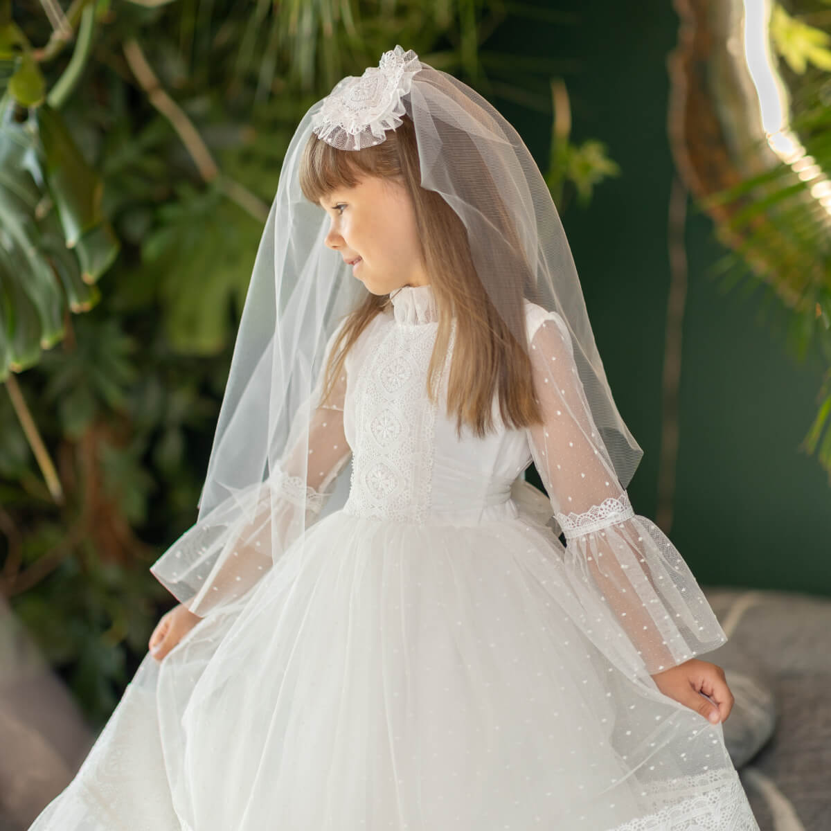 Young girl in a white dress with a First Communion Veil standing outdoors.