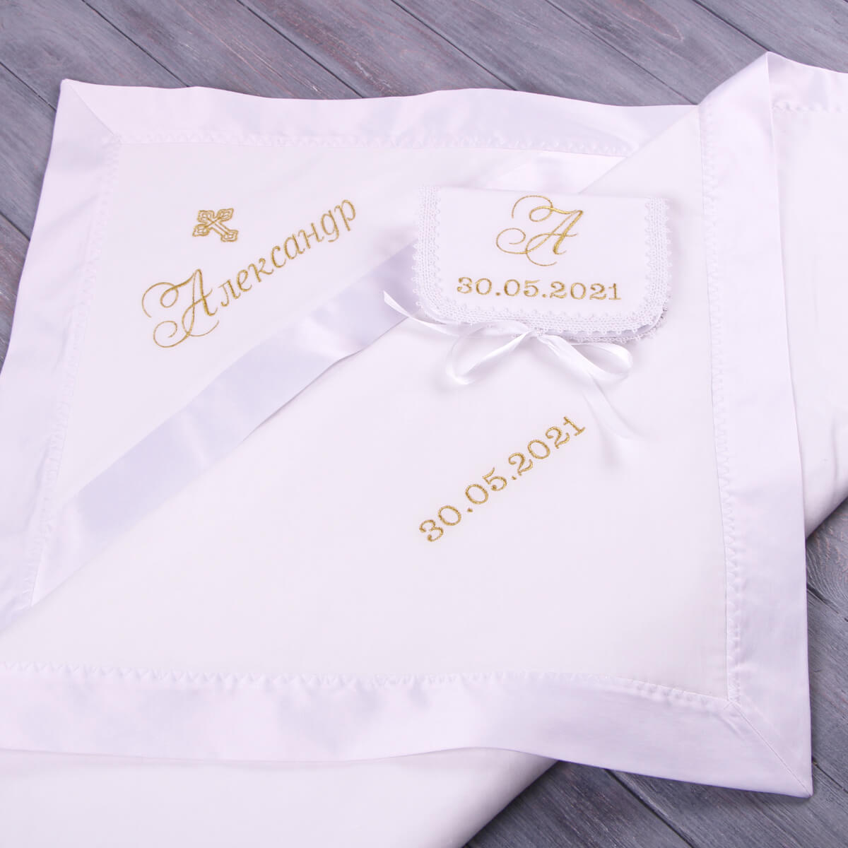 White ivory baptism blanket with embroidered name and date on a wooden surface