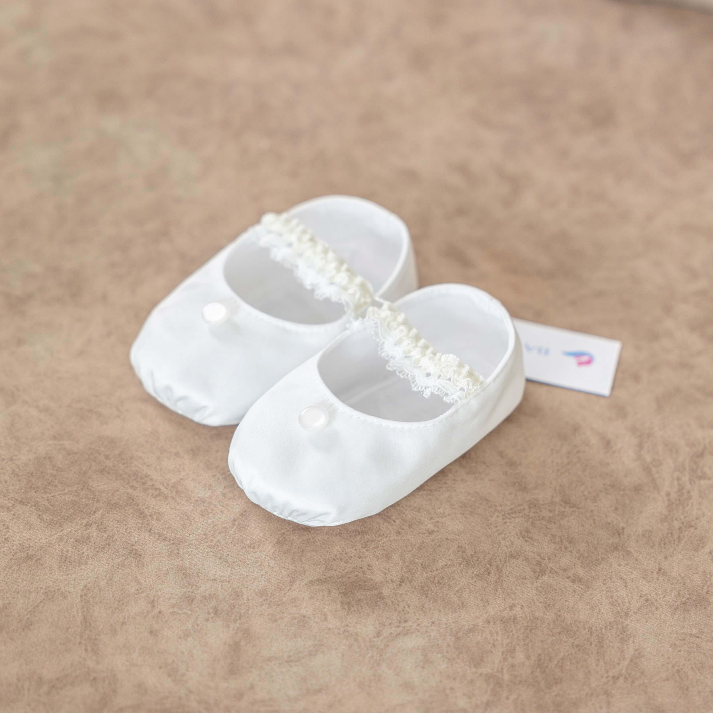  Christening Booties with a decorative bow on a beige surface