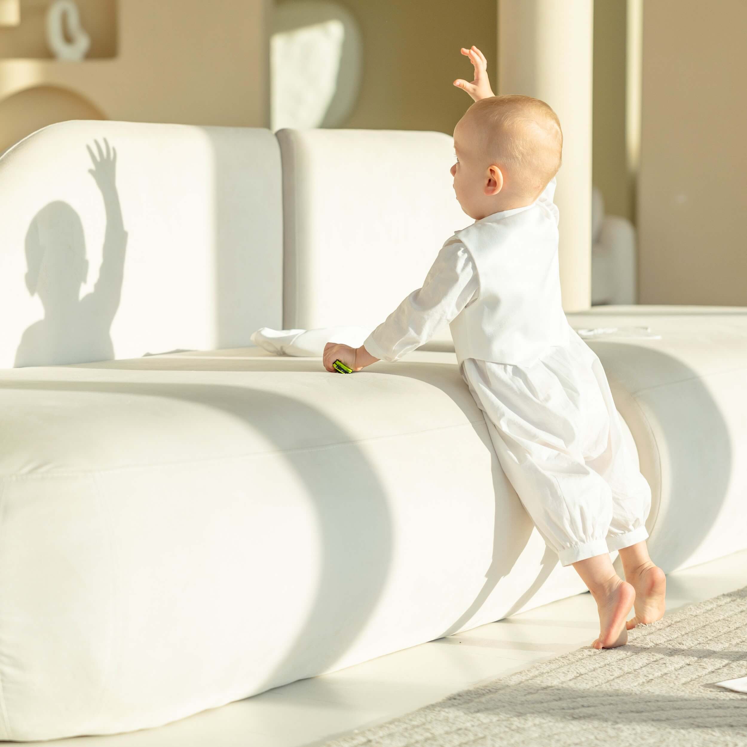 Child playing on a modern white chair in Baby Boy Baptism Romper with a neutral background