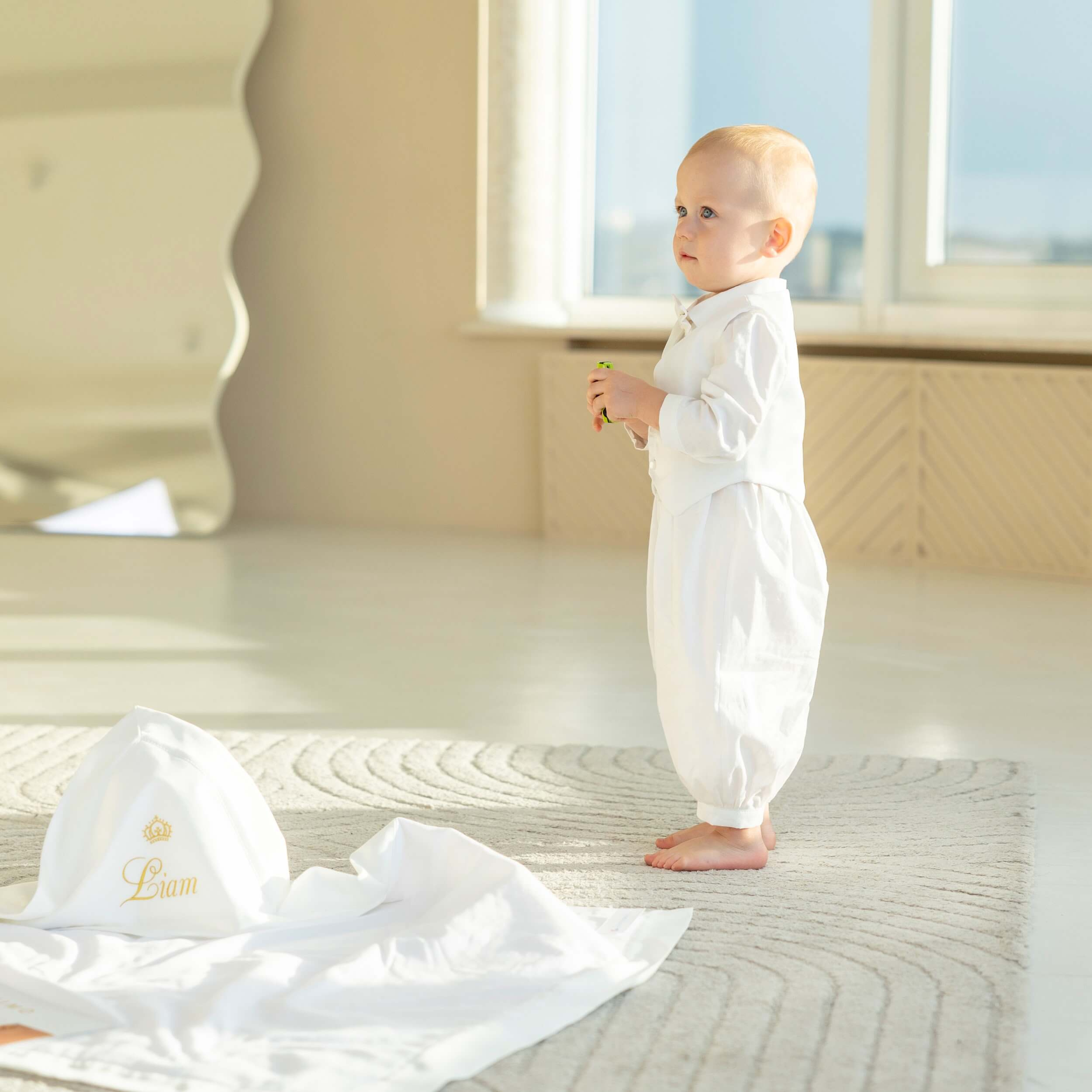 Baby in a Baby Boy Baptism Romper standing in a bright room with a L'ovediva towel.