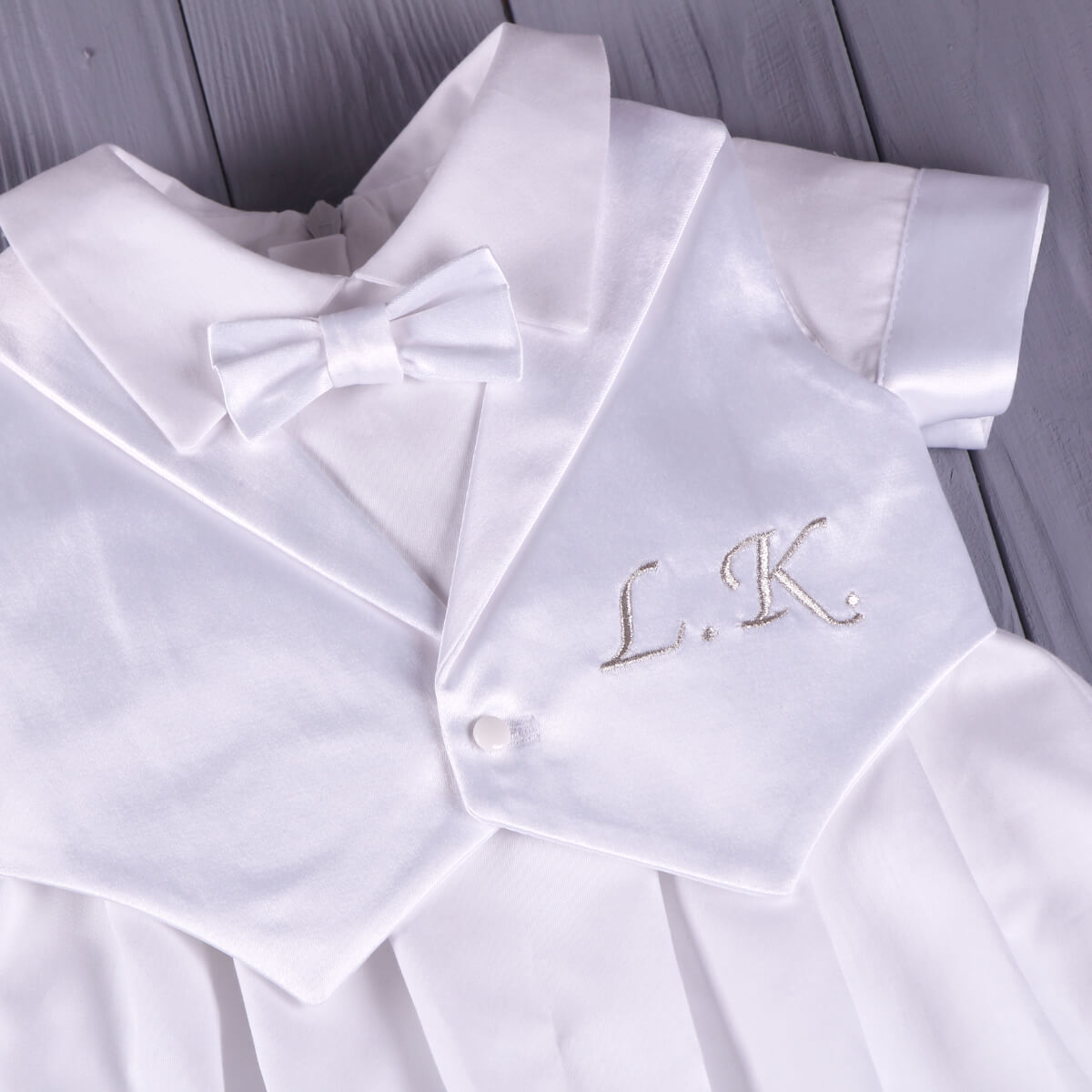 Baby Boy Baptism Romper and handkerchief with 'L.K.' embroidery on a wooden surface
