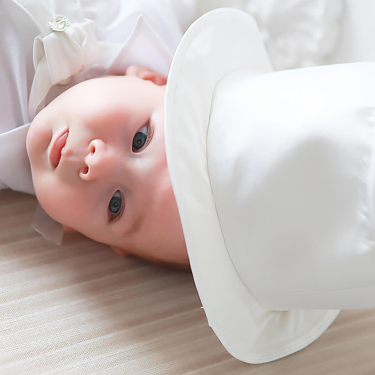 Newborn baby lying on a wooden floor wearing a Boy Christening Hat.