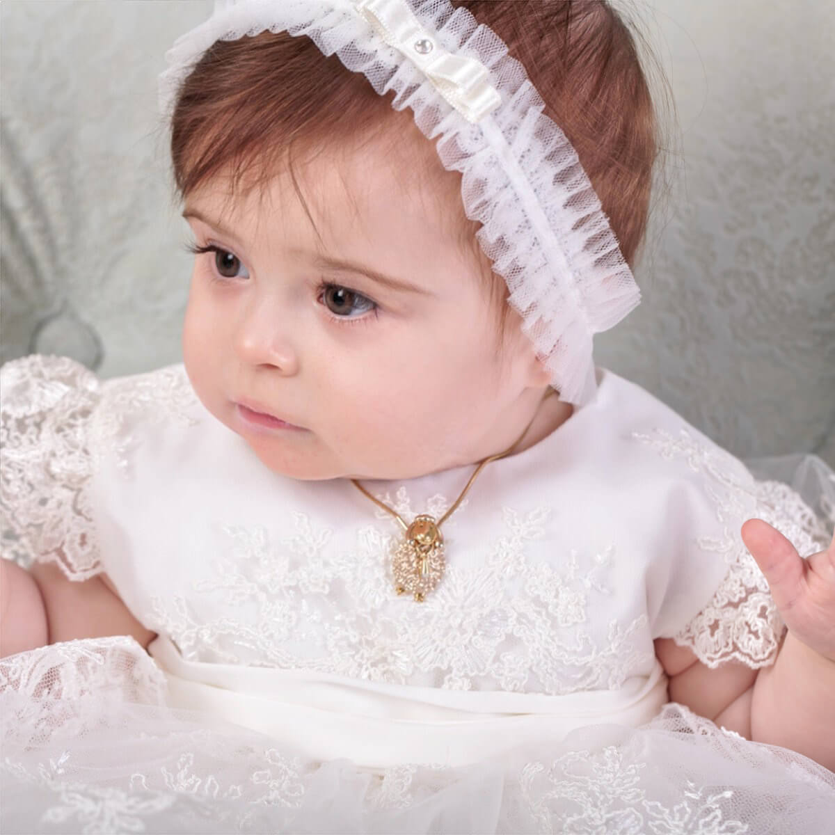 Baby in a Elegant Christening Dress with a headband, sitting on a soft surface.