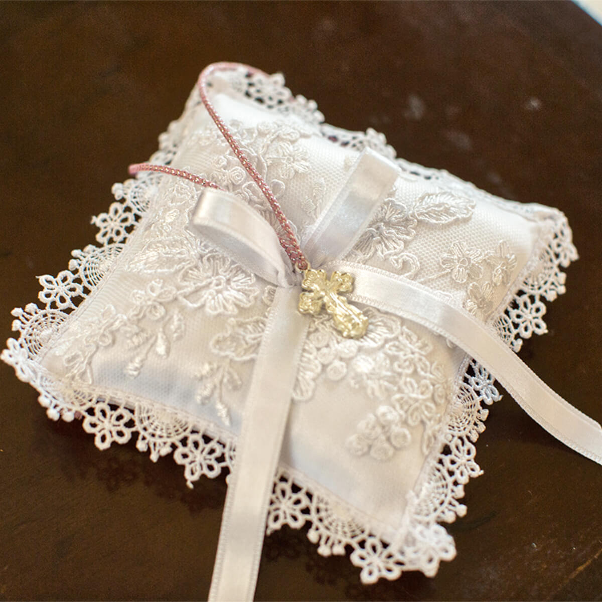 Baptism Ceremony Pillow with a white ribbon on a wooden surface
