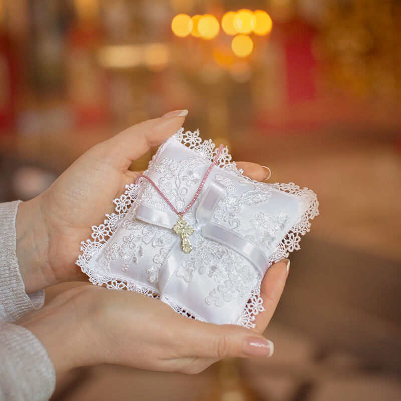 Baptism Ceremony Pillow with a bow held by hands against a blurred background