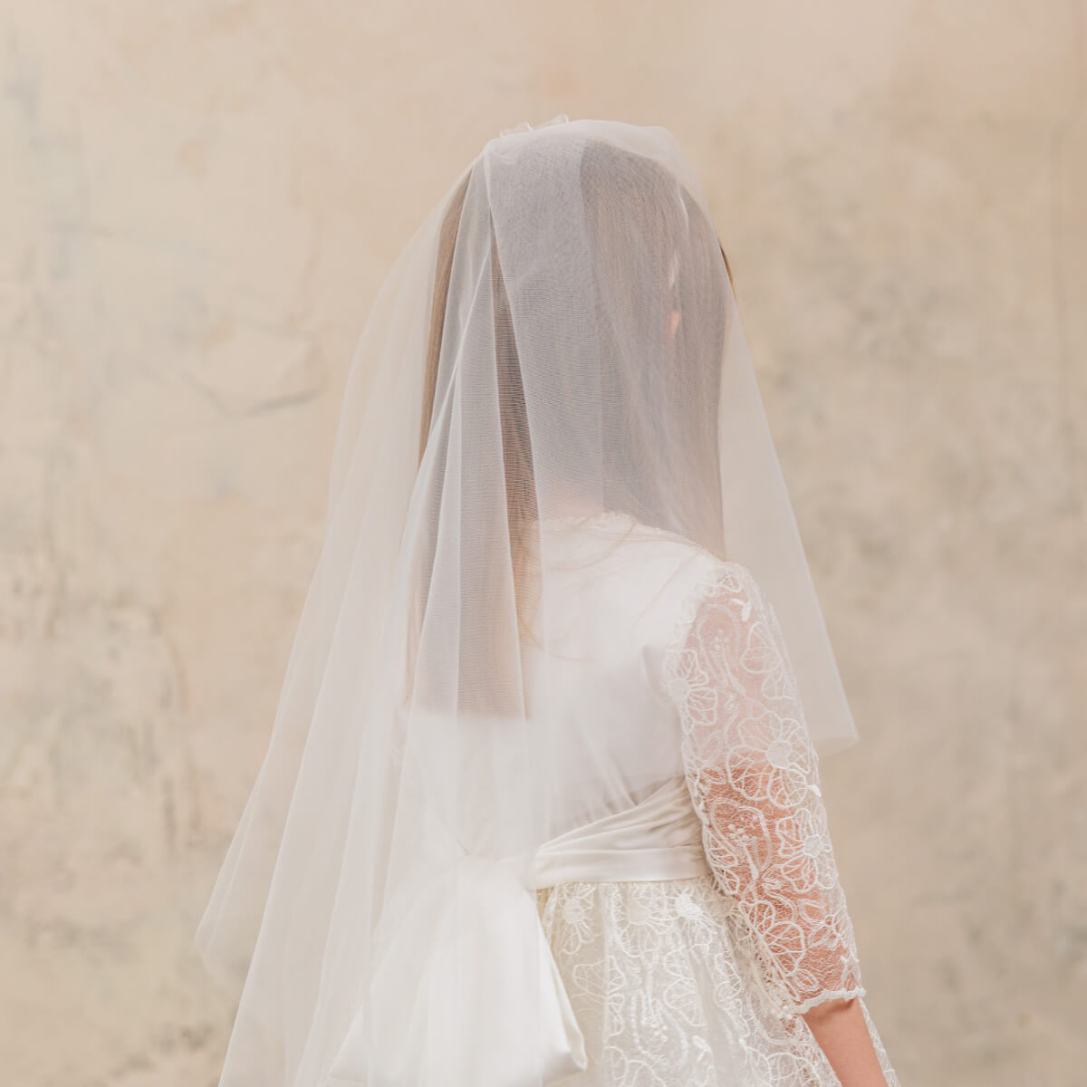 Person wearing a First Communion Dress with a sheer veil against a beige background