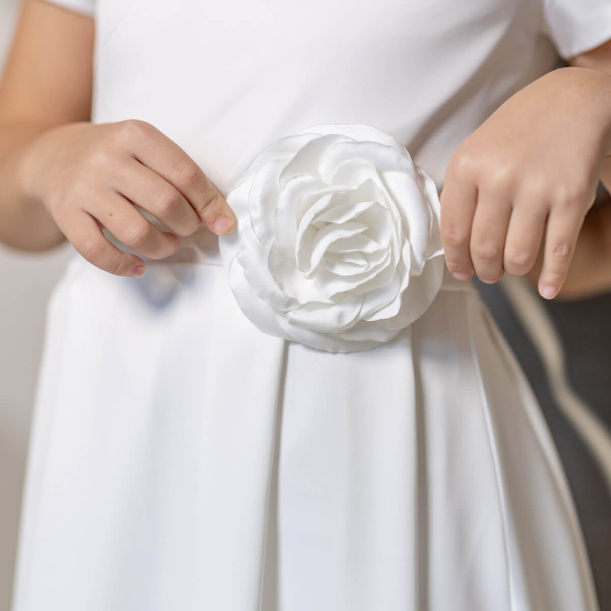 White dress with a large floral bow detail, held by hands.