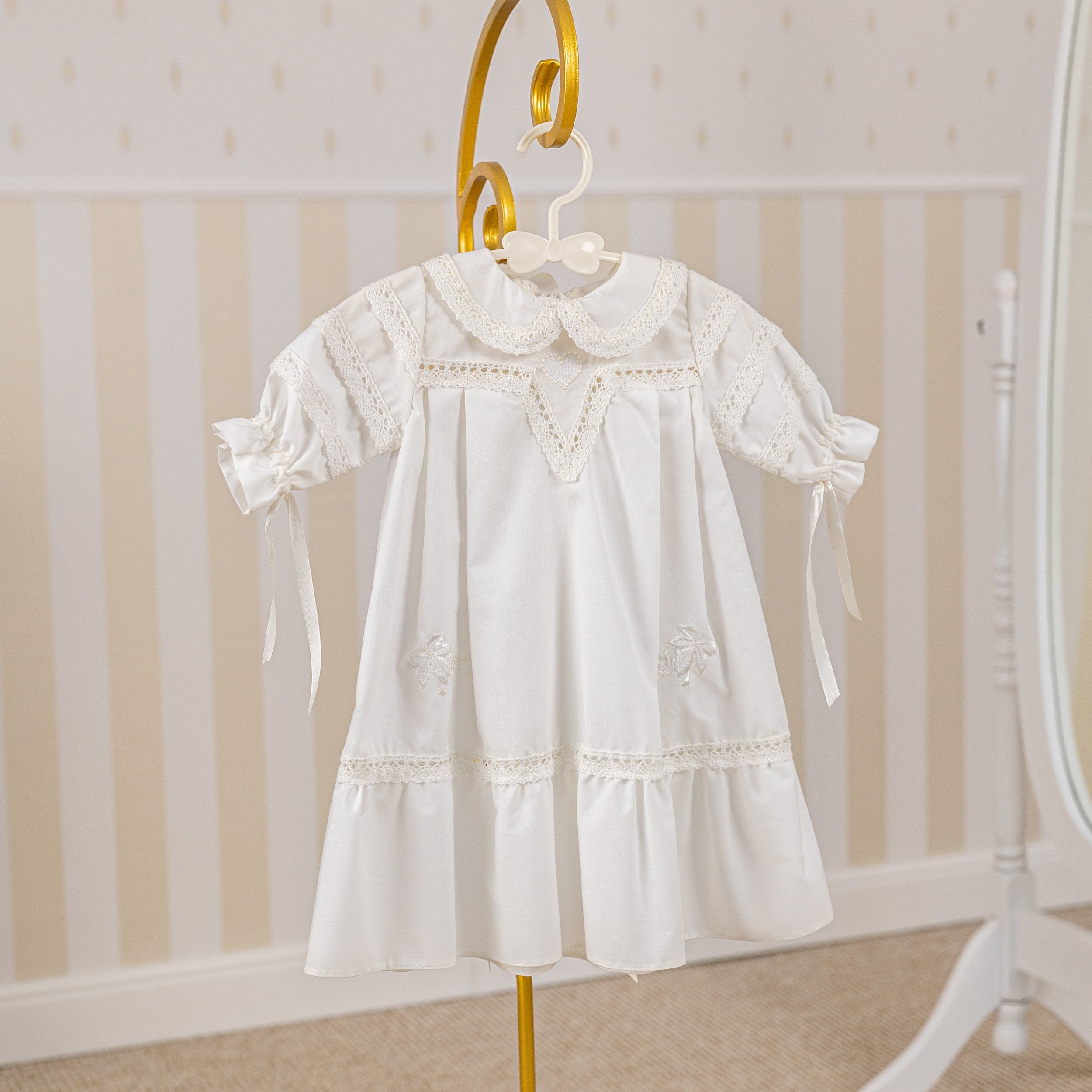 Girls Baptism Gown with lace details on a hanger against a striped wall.
