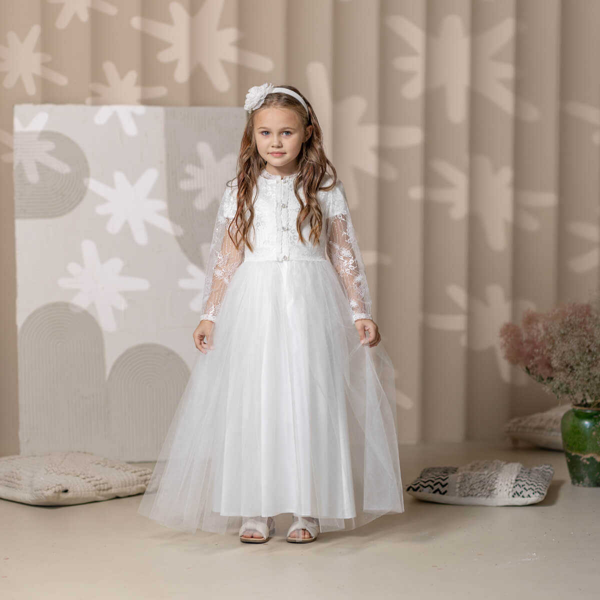 Young girl in a white Catholic Communion Dress standing in a softly lit room with decorative elements.