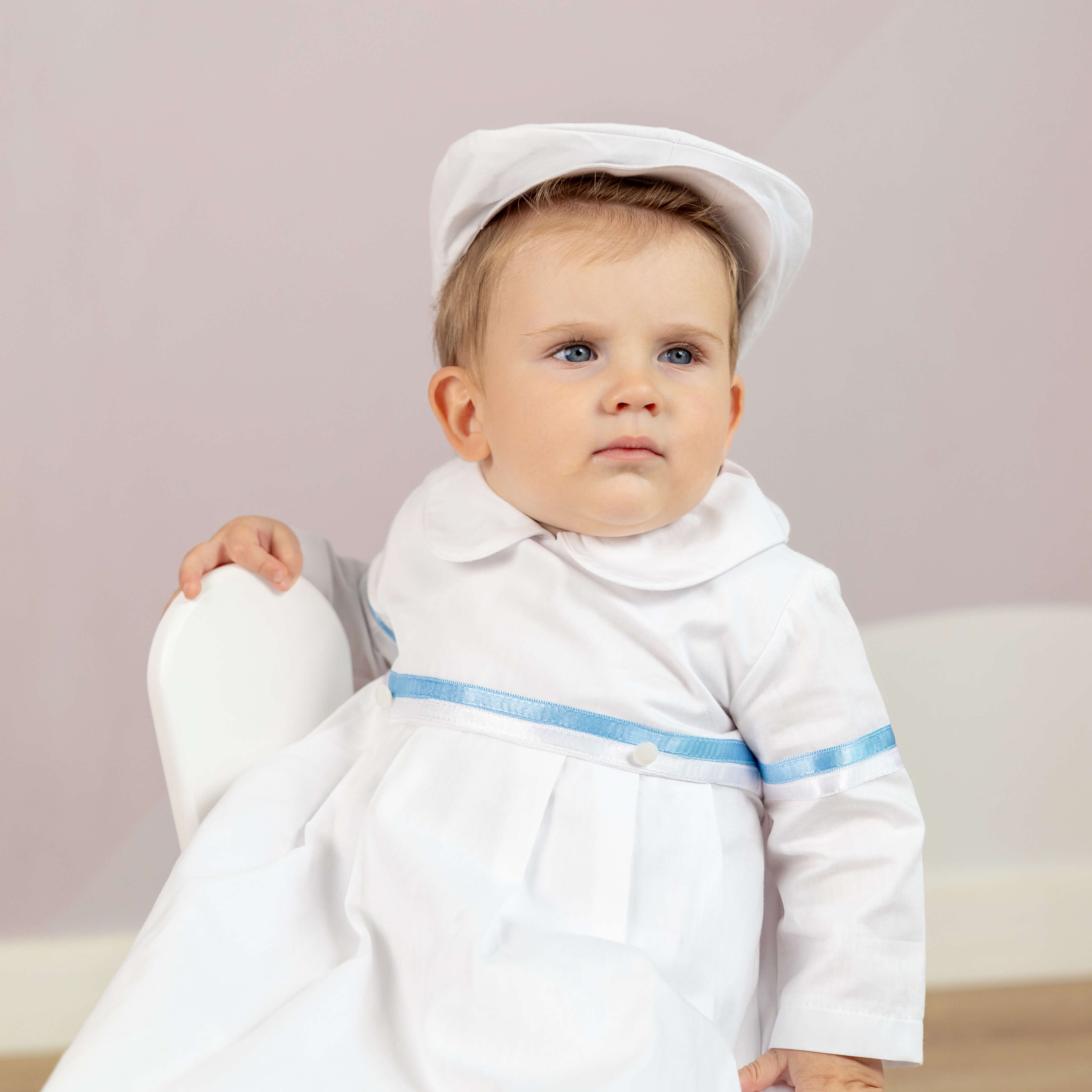 Baby in a white outfit with a hat on a light background