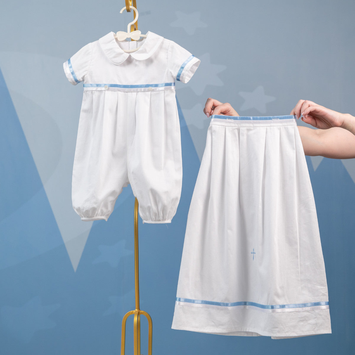 White baby outfit with blue trim on a hanger against a blue background