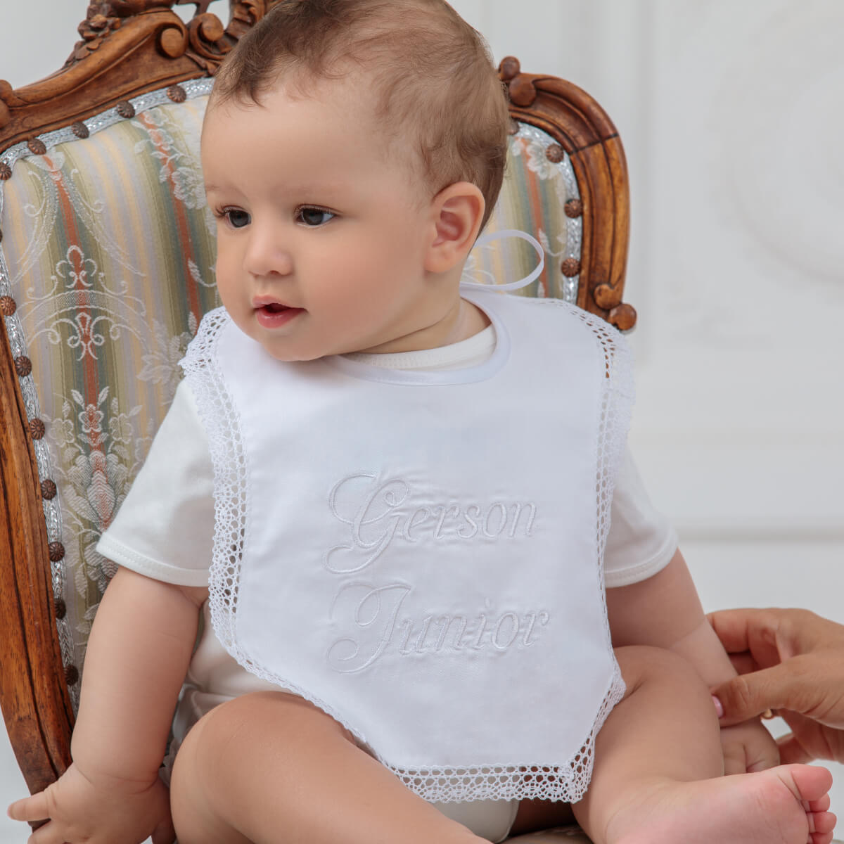 Baby wearing a Newborn Bib  with embroidered text, sitting on a wooden chair.