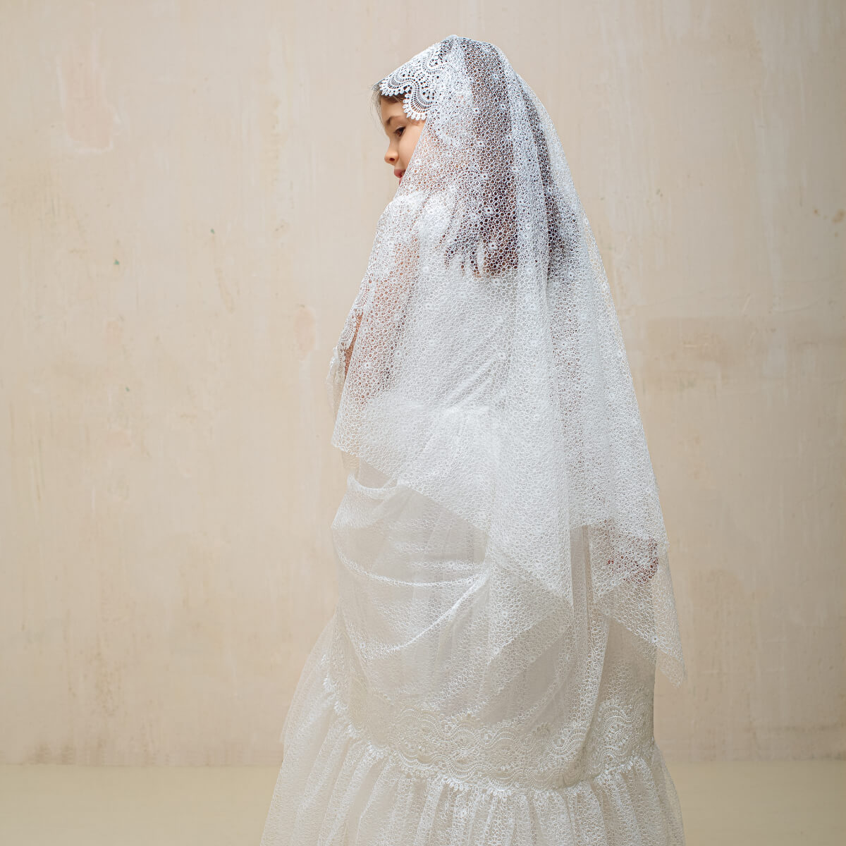 Woman wearing a lace veil against a plain background