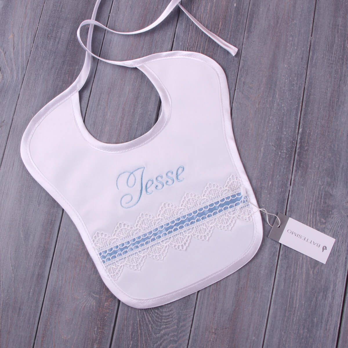 Baptism Bib with blue lace details and embroidered name 'Jesse' on a wooden surface