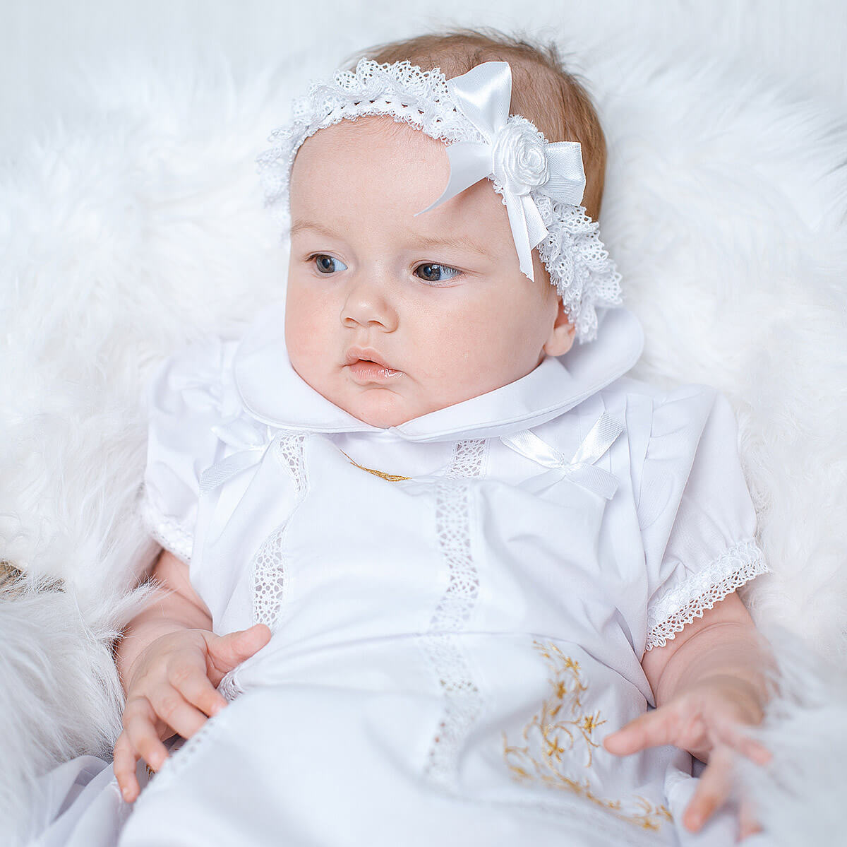Baby in a White Christening Dress with lace details and a headband on a white background