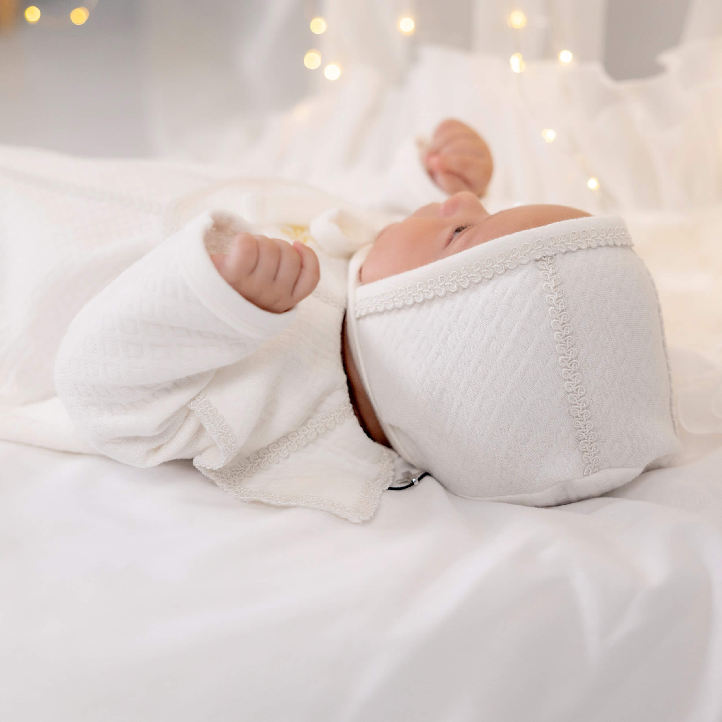 Newborn baby wrapped in Baby Boy Christening Romper with blurred lights in the background
