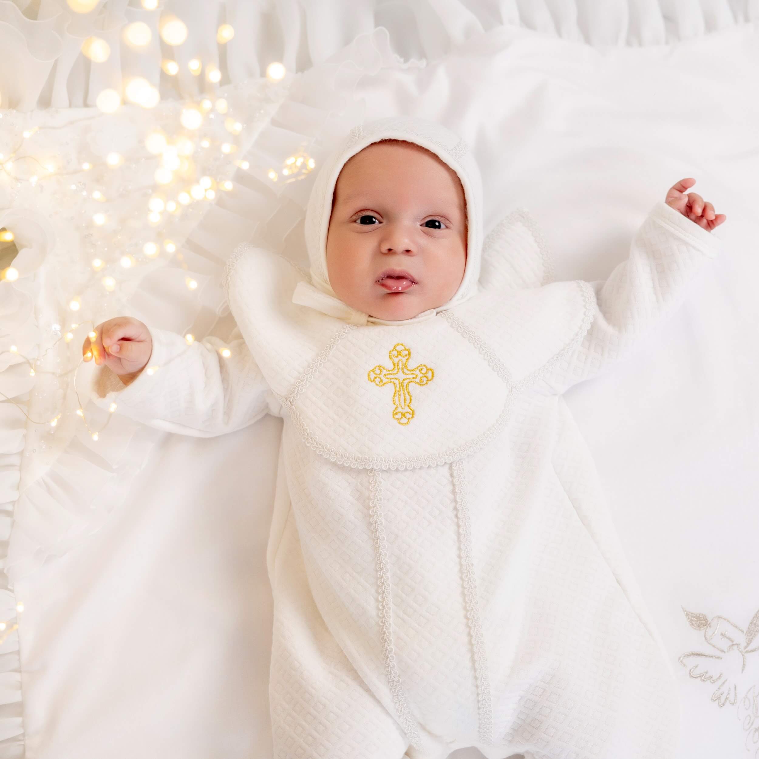 Baby in a Baby Boy Christening Romper with a gold cross, surrounded by soft lighting