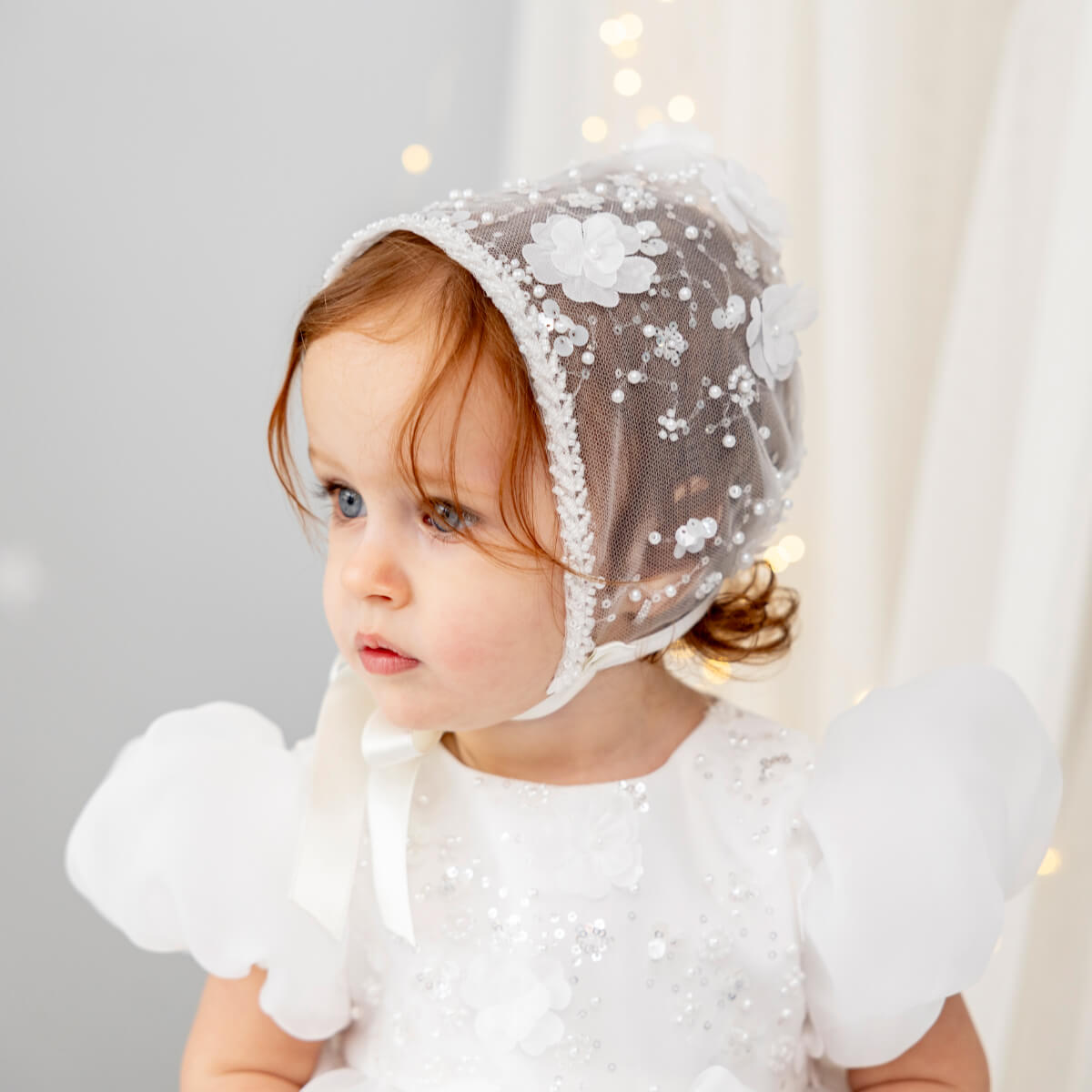 Child wearing a Lace Christening Bonnet with floral details against a neutral background