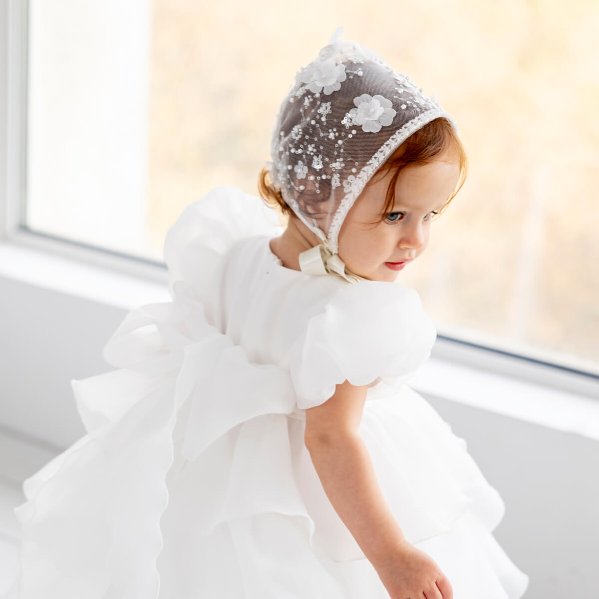 Child wearing a Lace Christening Bonnet in a softly lit room.