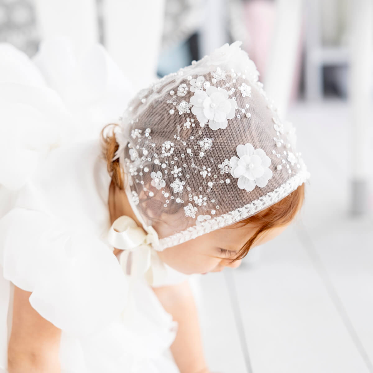 Child wearing a Lace Christening Bonnet with floral embellishments on a blurred background