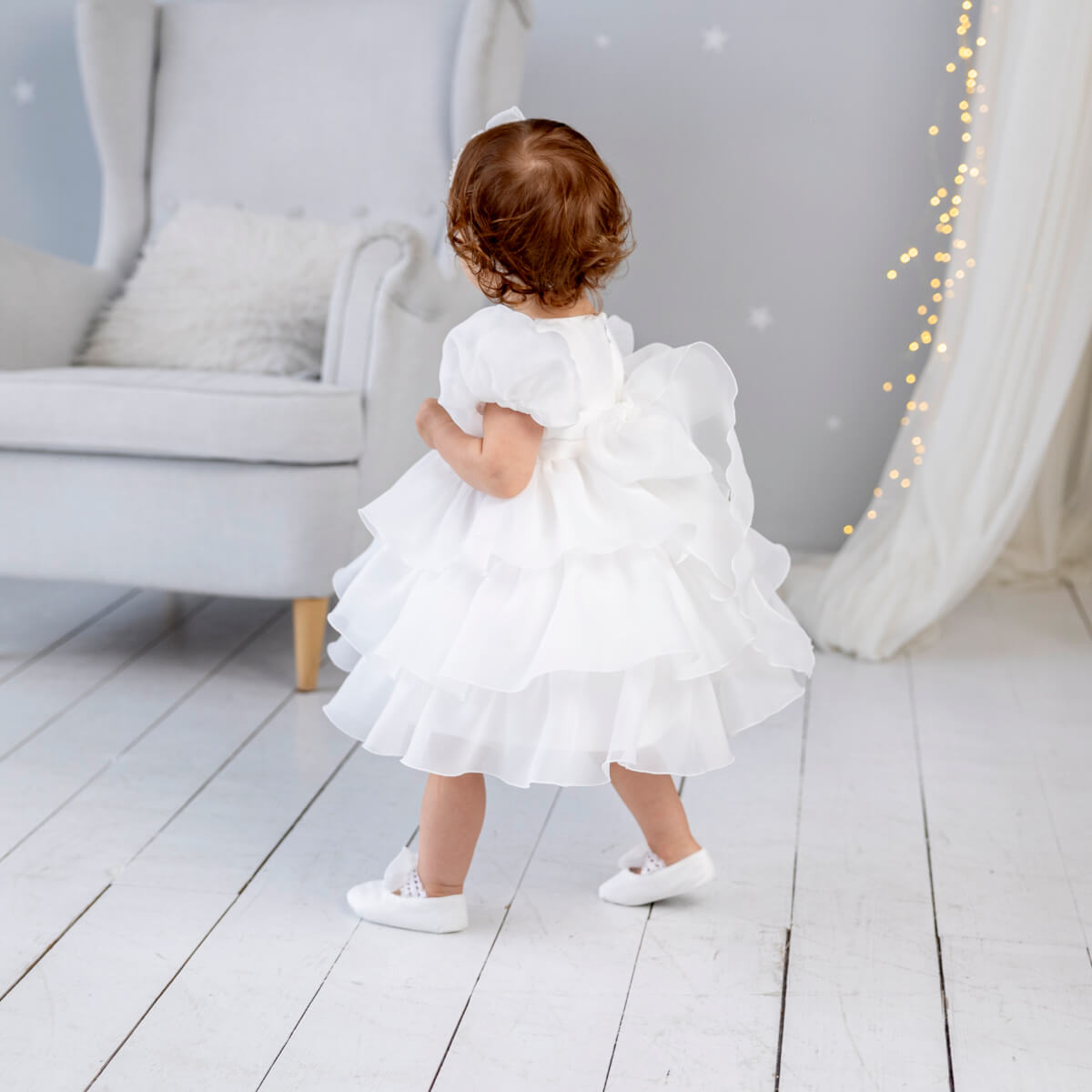 Child in a Baptism Dress with Detachable Train standing on a light wooden floor with a neutral background.