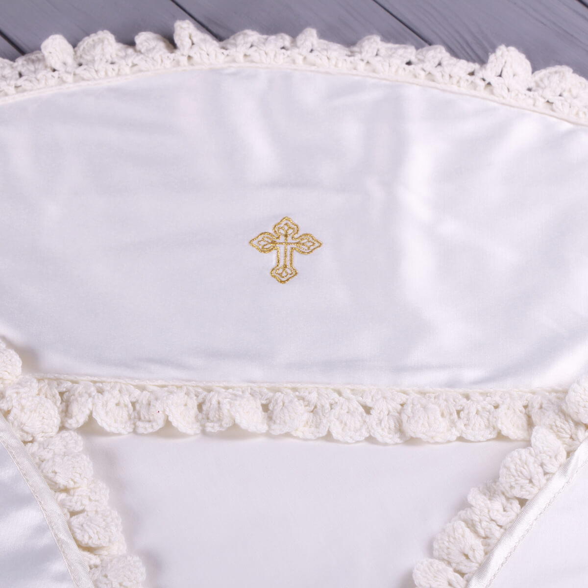 White embroidered cross on a baptism blanket  with lace trim against a wooden background