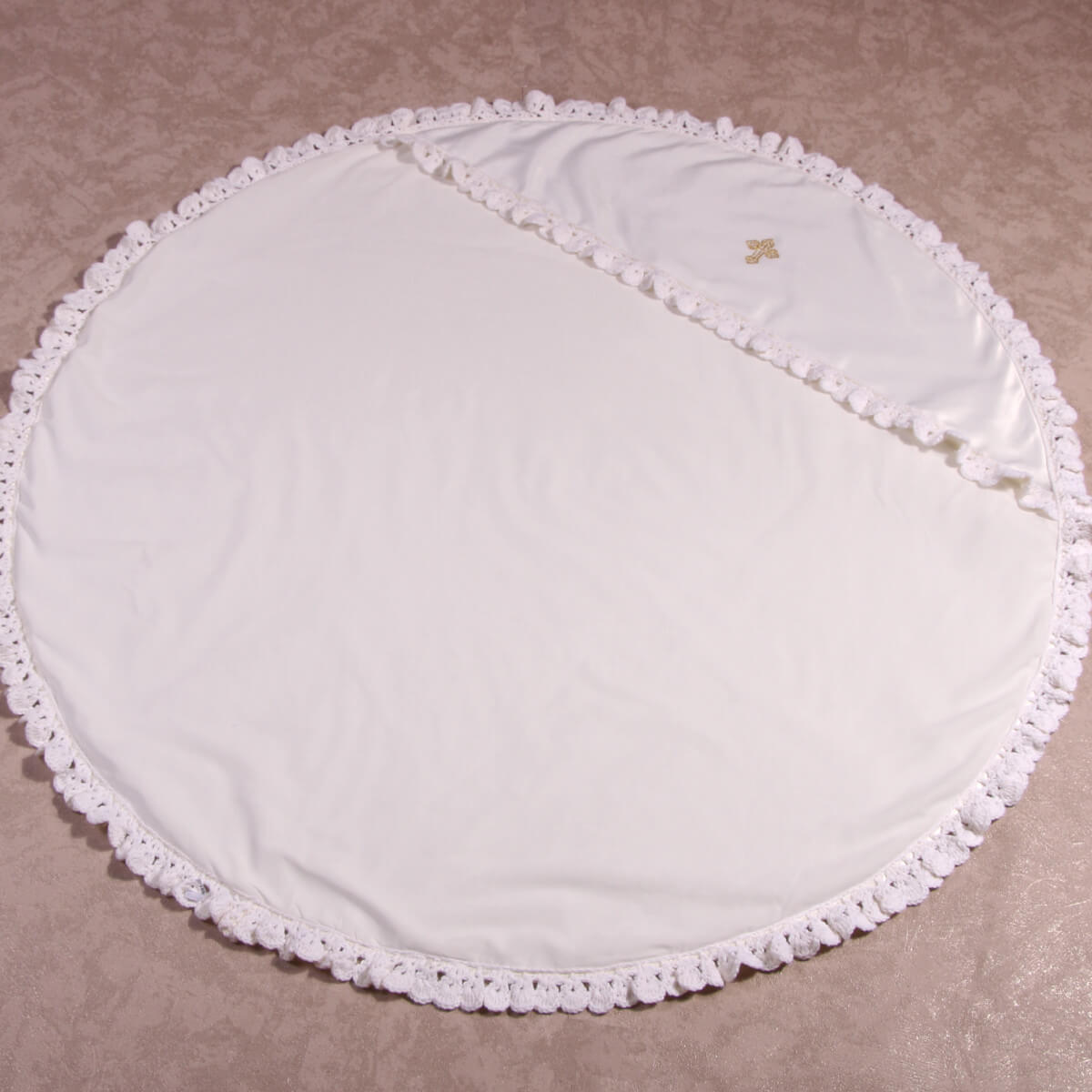 Round white baptism blanket with lace trim on a beige background