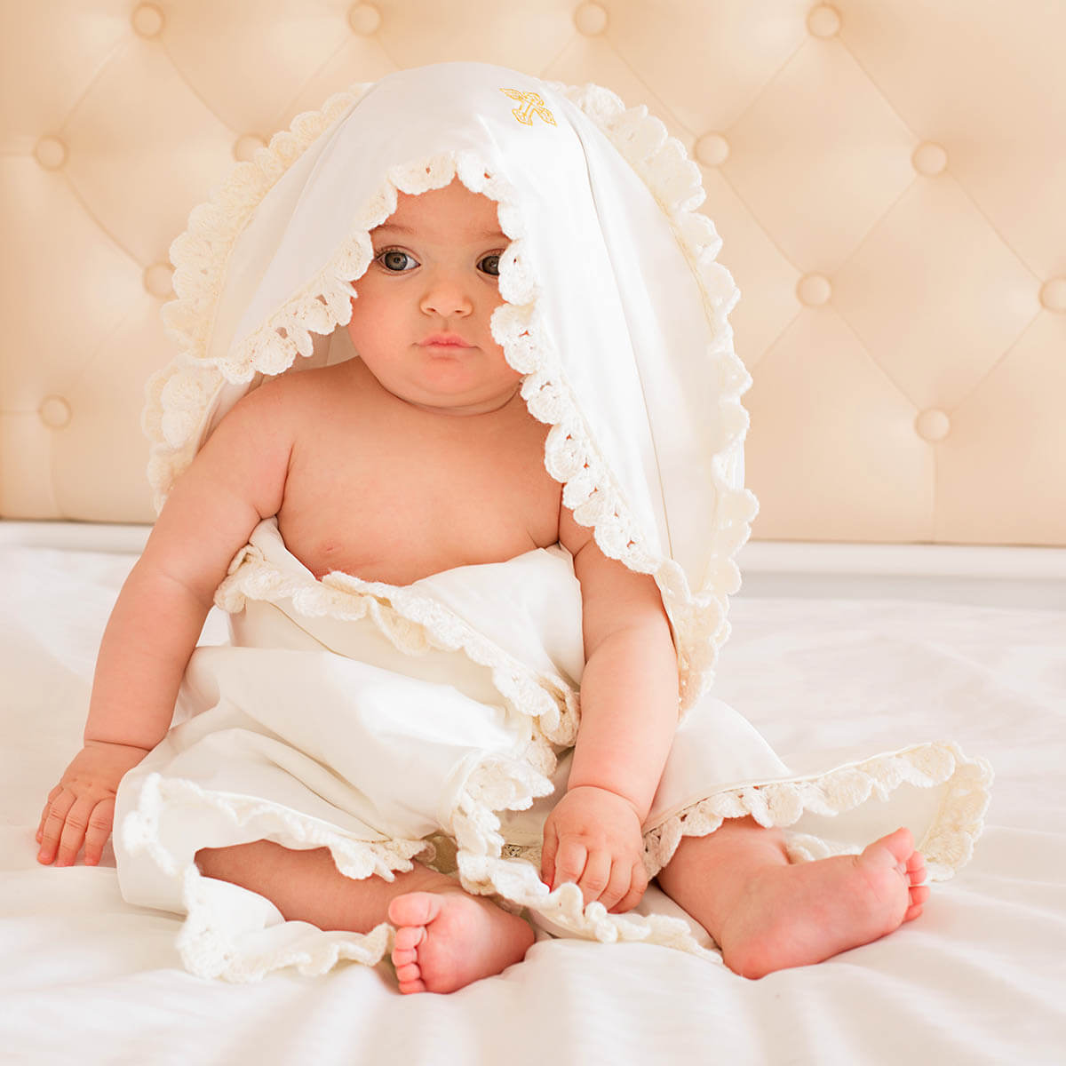 Baby wrapped in a white lace blanket on a beige background