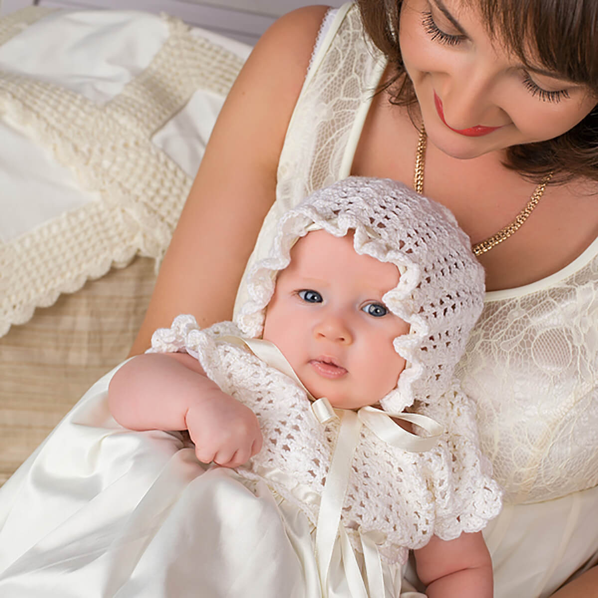 Woman holding a baby wearing a Crochet Christening Bonnet in a soft, warm setting.