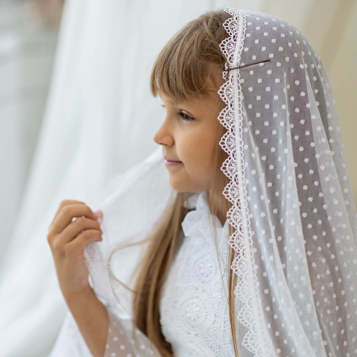 Young girl wearing a white pFirst Communion Mantilla Veil with lace trim.