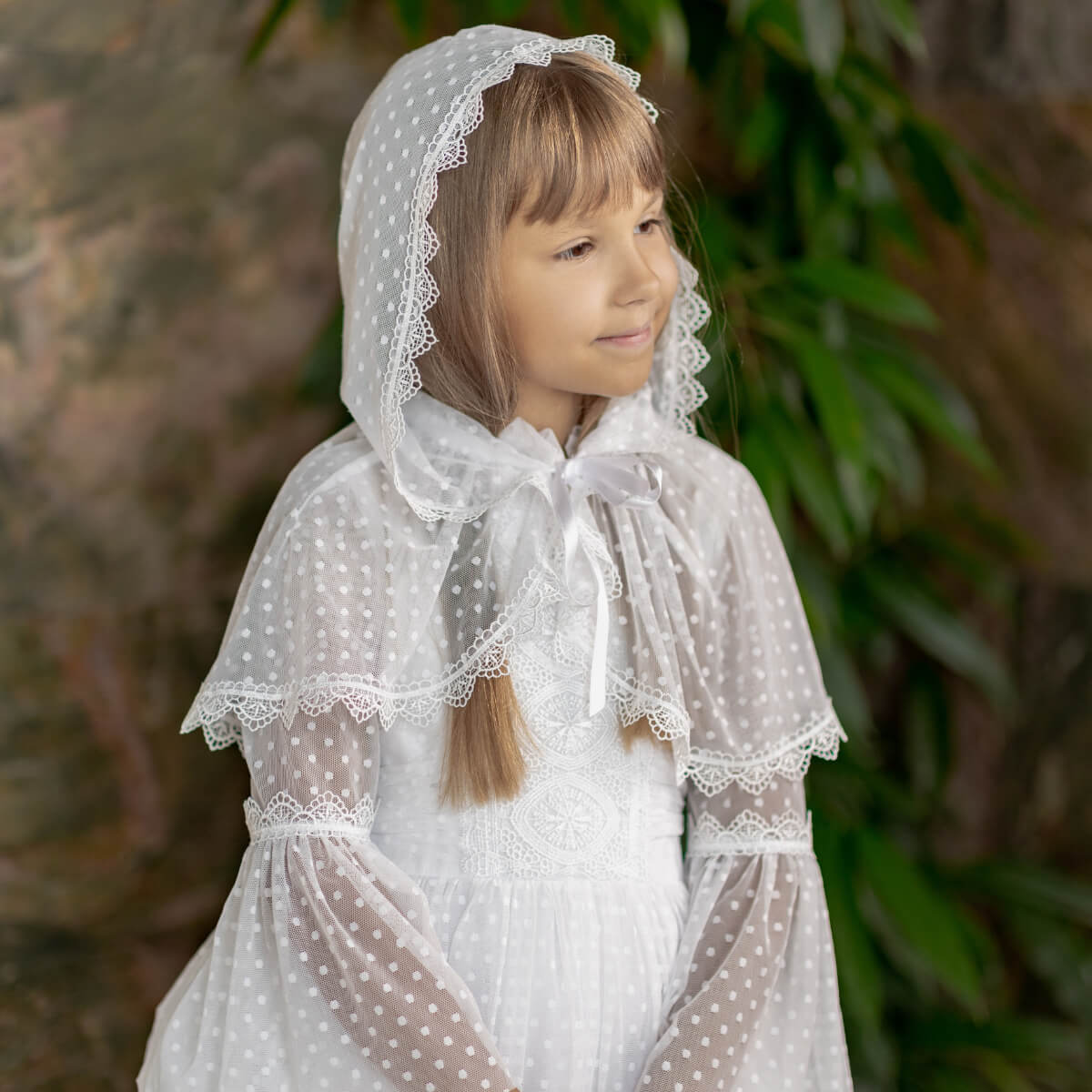 Young girl wearing a white polka dot dress with a First Communion Mantilla Veil against a natural background